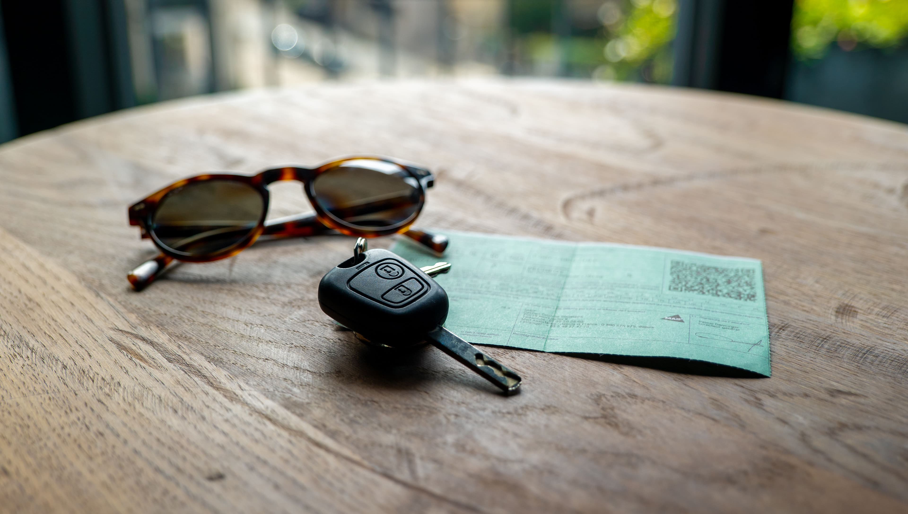 Sur une table, une clé de voiture, une carte verte d'assurance auto et des lunettes de soleil