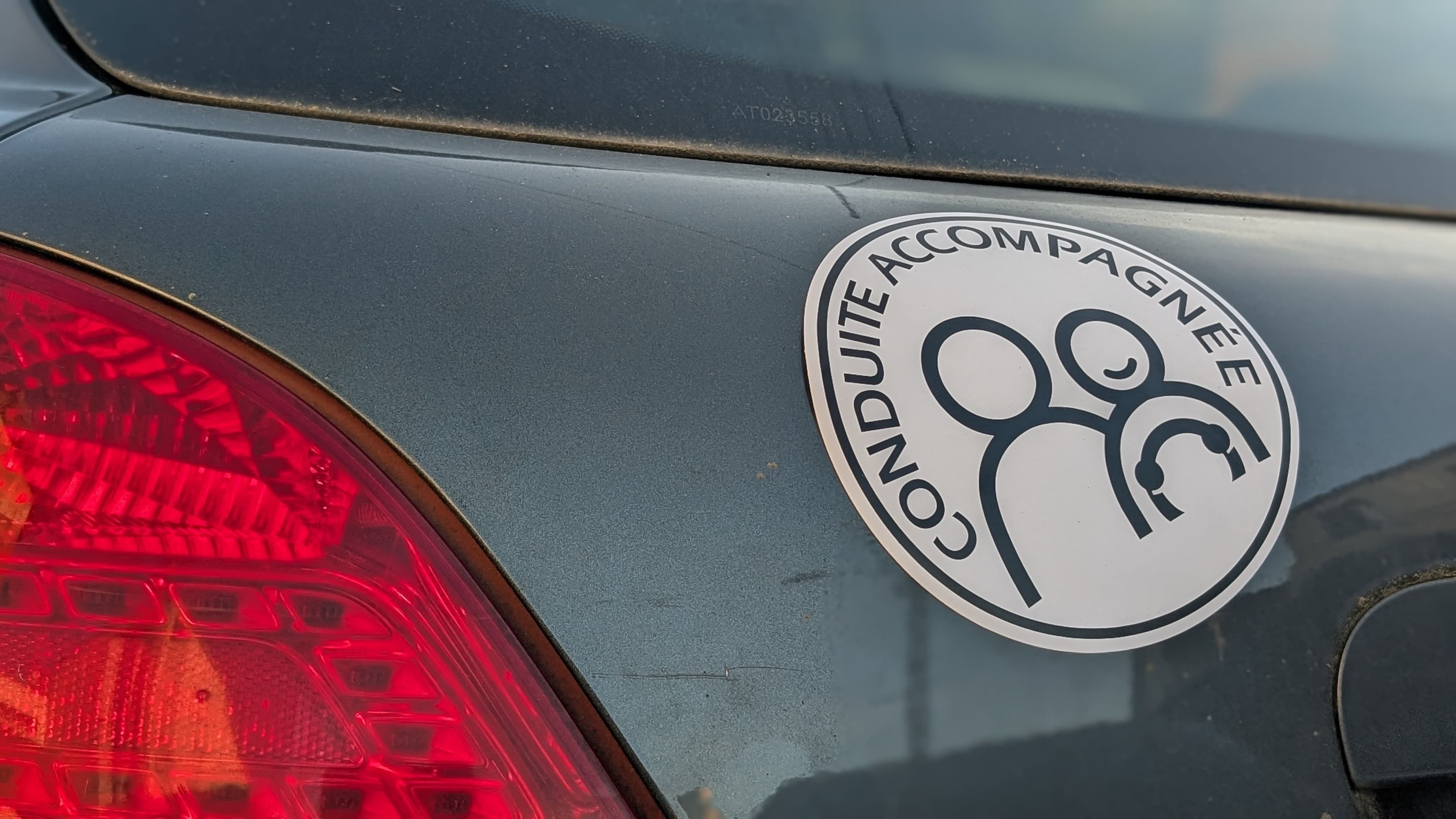 Un autocollant conduite accompagnée AAC collé à l'arrière d'une voituer grise
