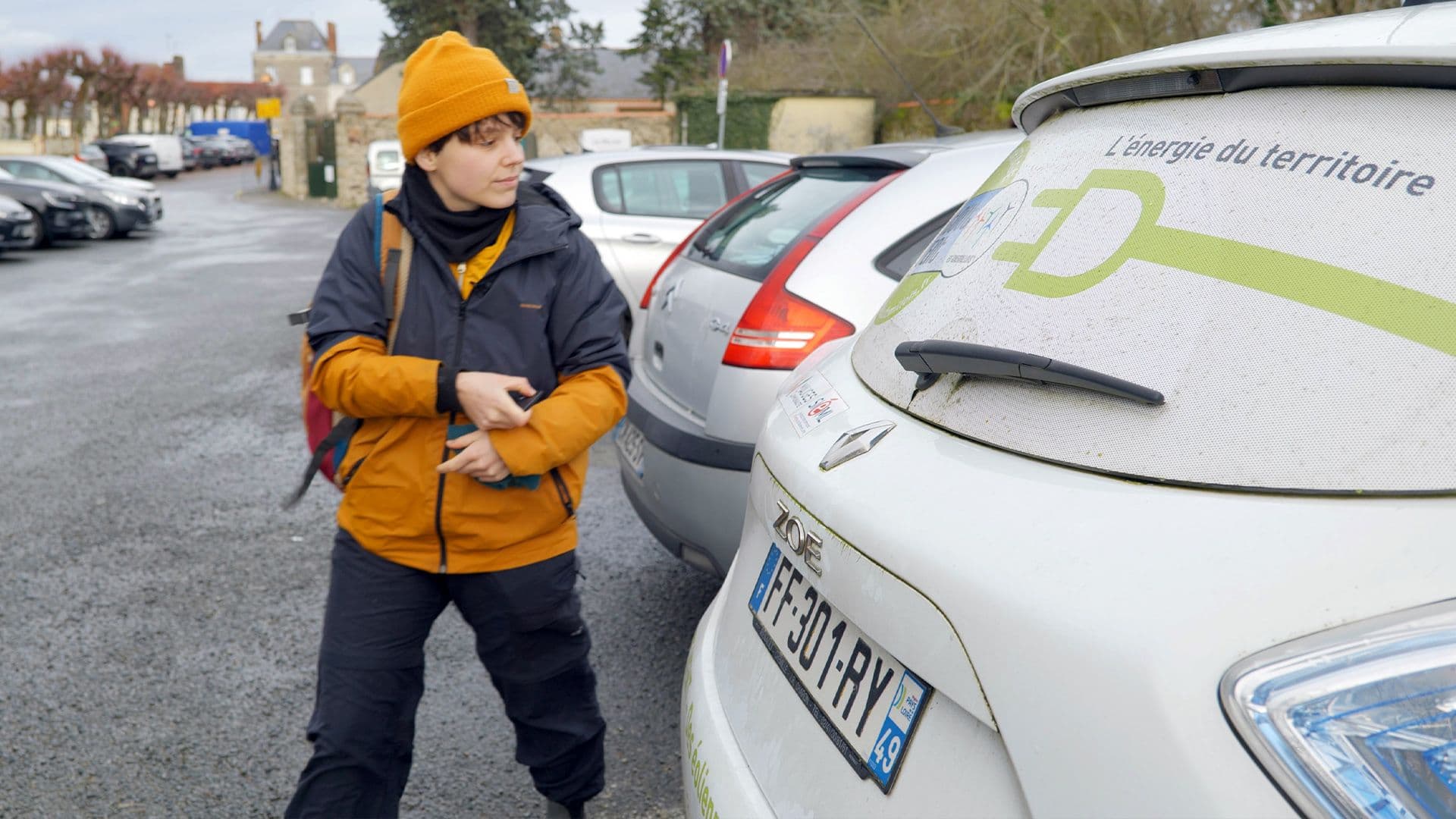 Une femme avecu n bonnet orange appuie sur la clé d'une voiture blanche pour la fermer