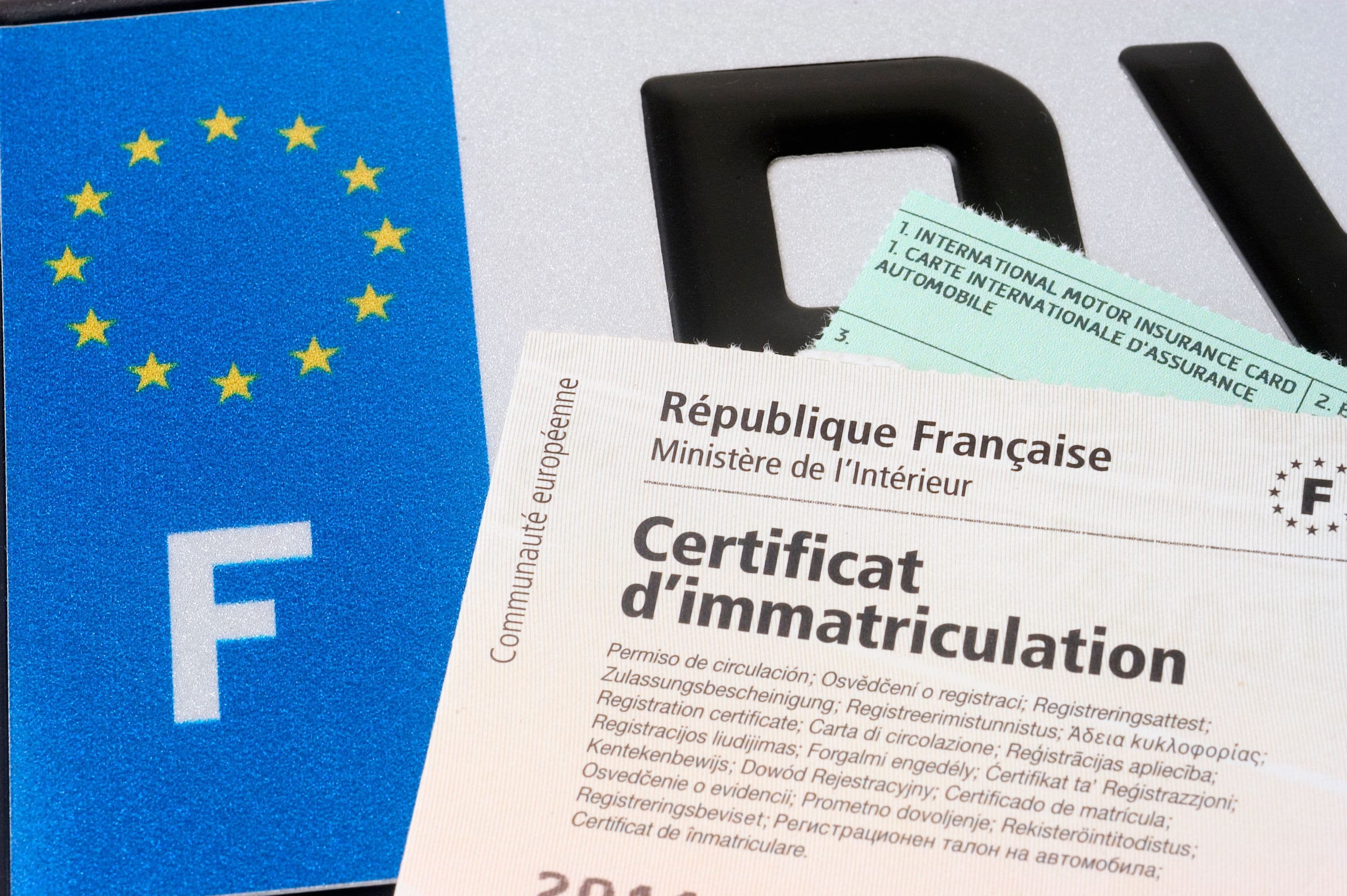 Une carte grise papier posée sur une plaque d'immatriculation française