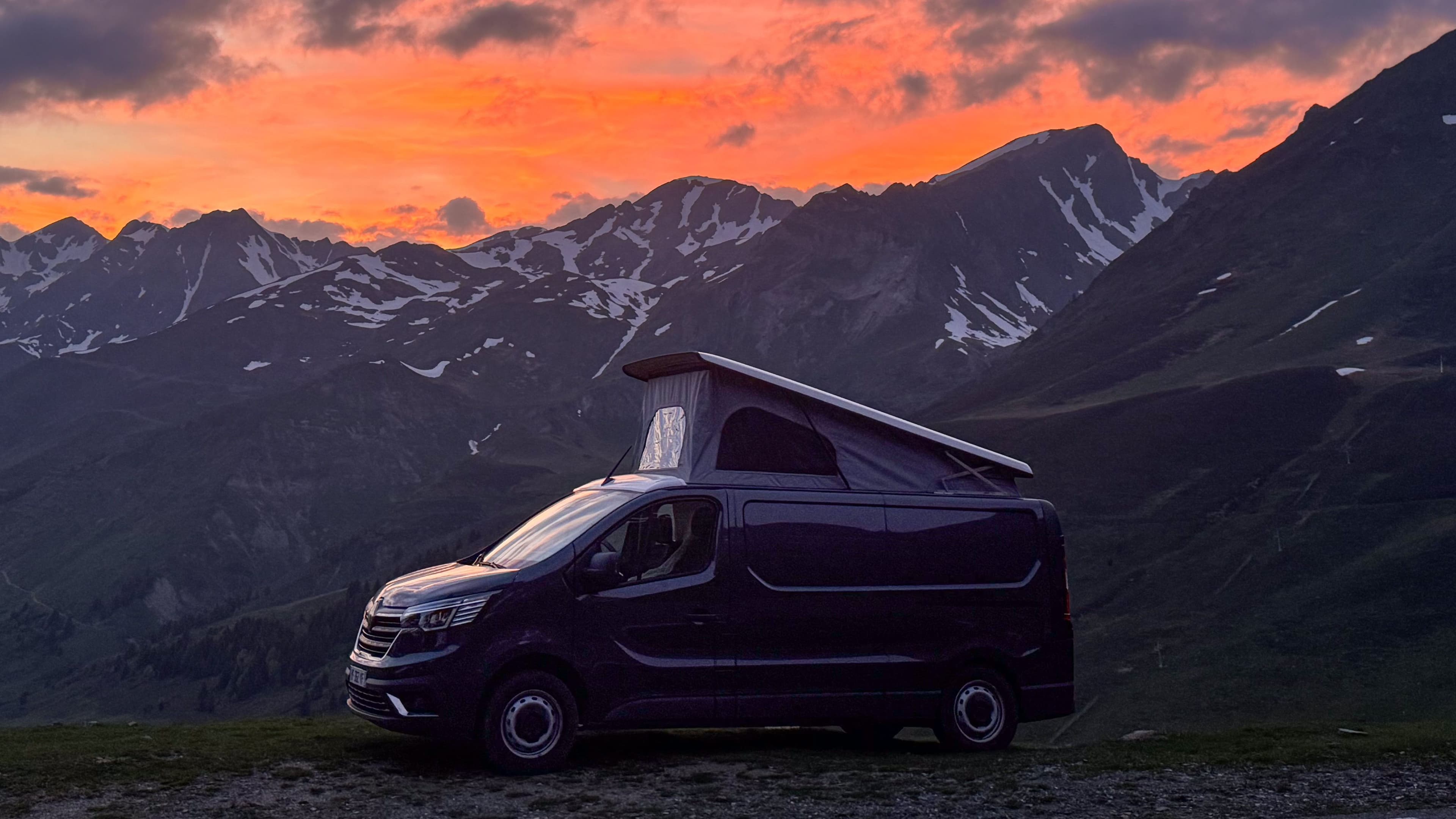 Un van aménagé devant un panorama de chaîne de montagne au coucher de soleil