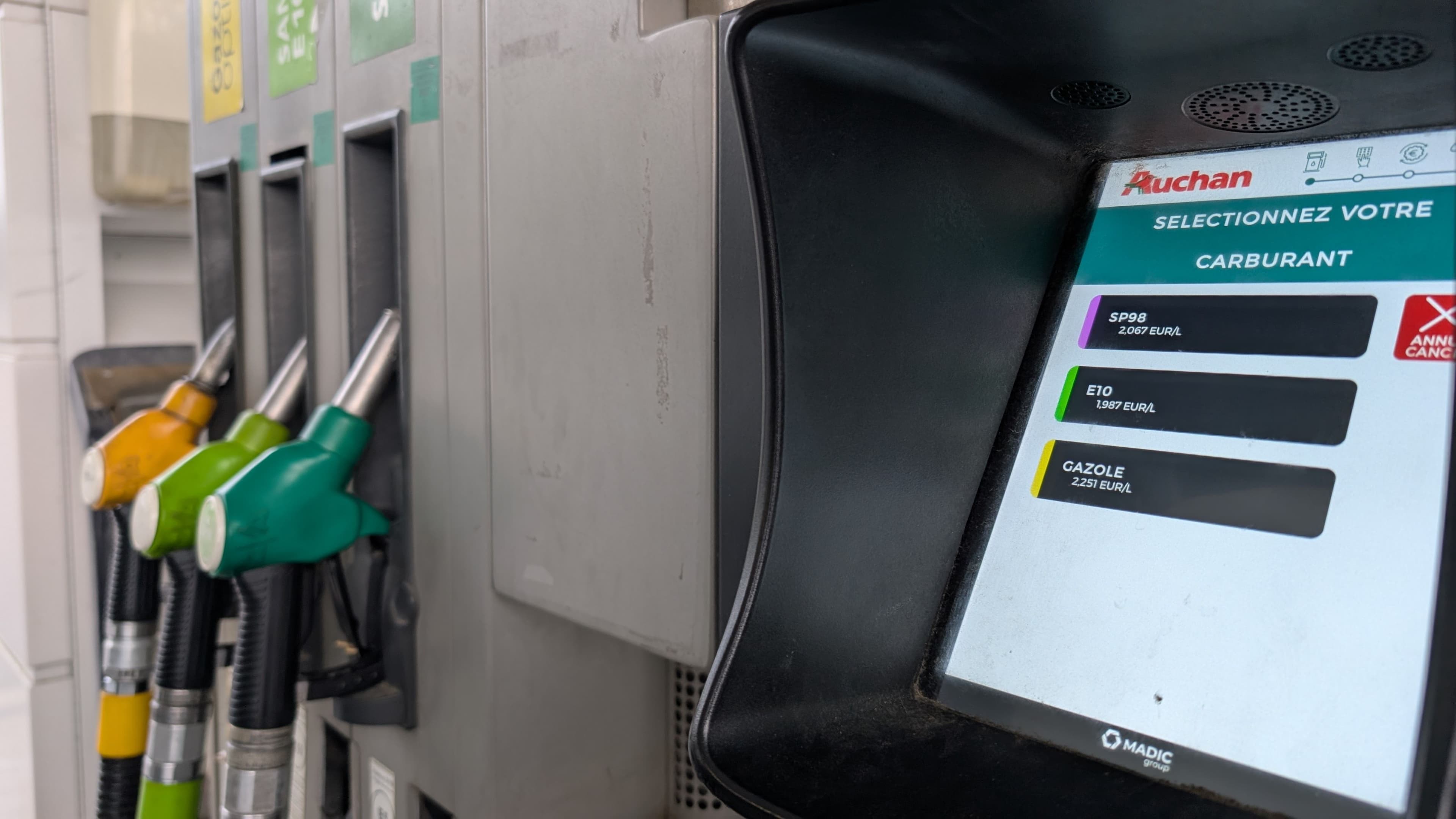 Un écran de station service montrant les prix des carburants gasoil, SP95 et SP98 et en arrière plan les pompes