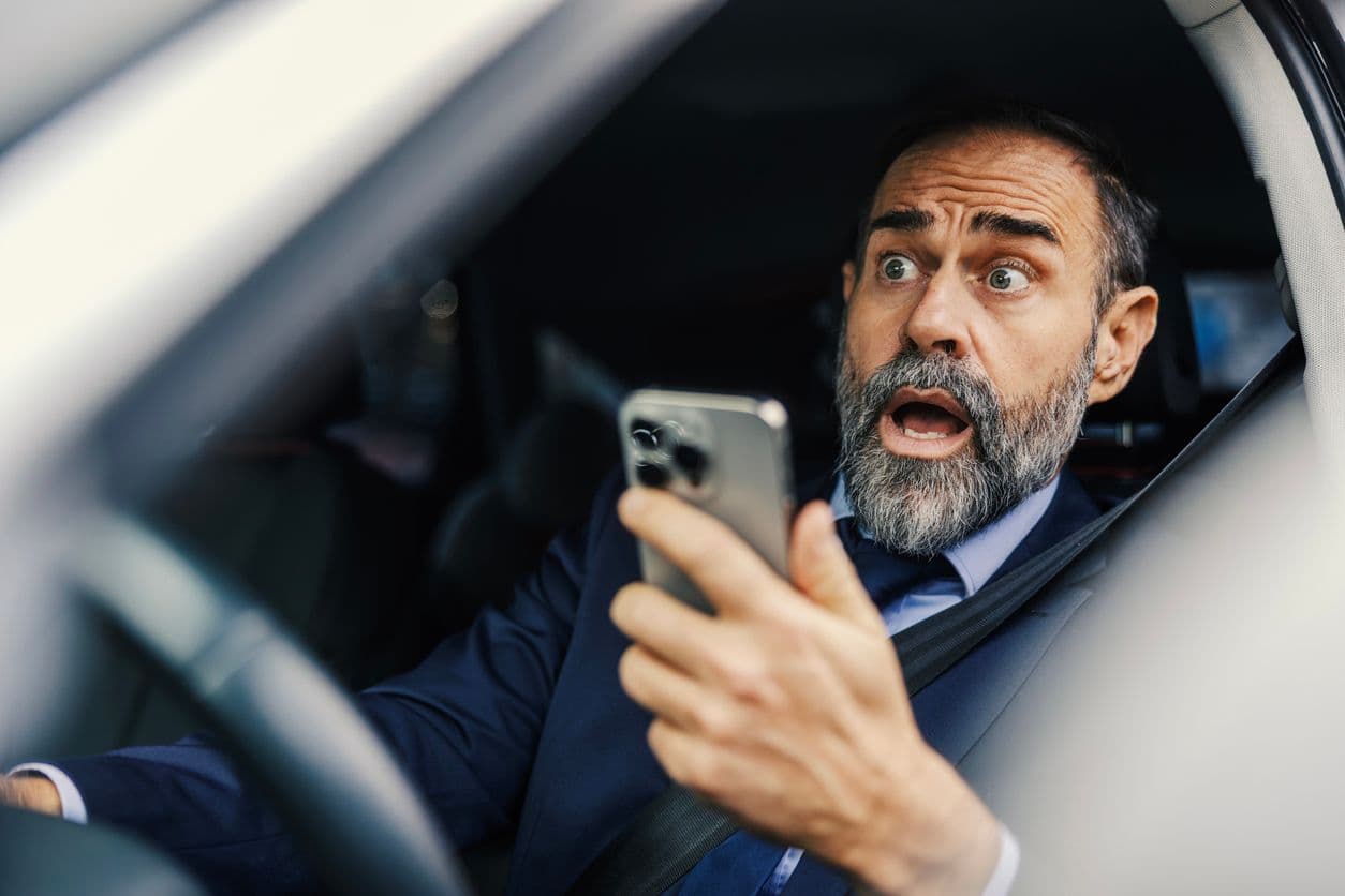 Un homme choqué avec un téléphone en main au volant de sa voiture. 