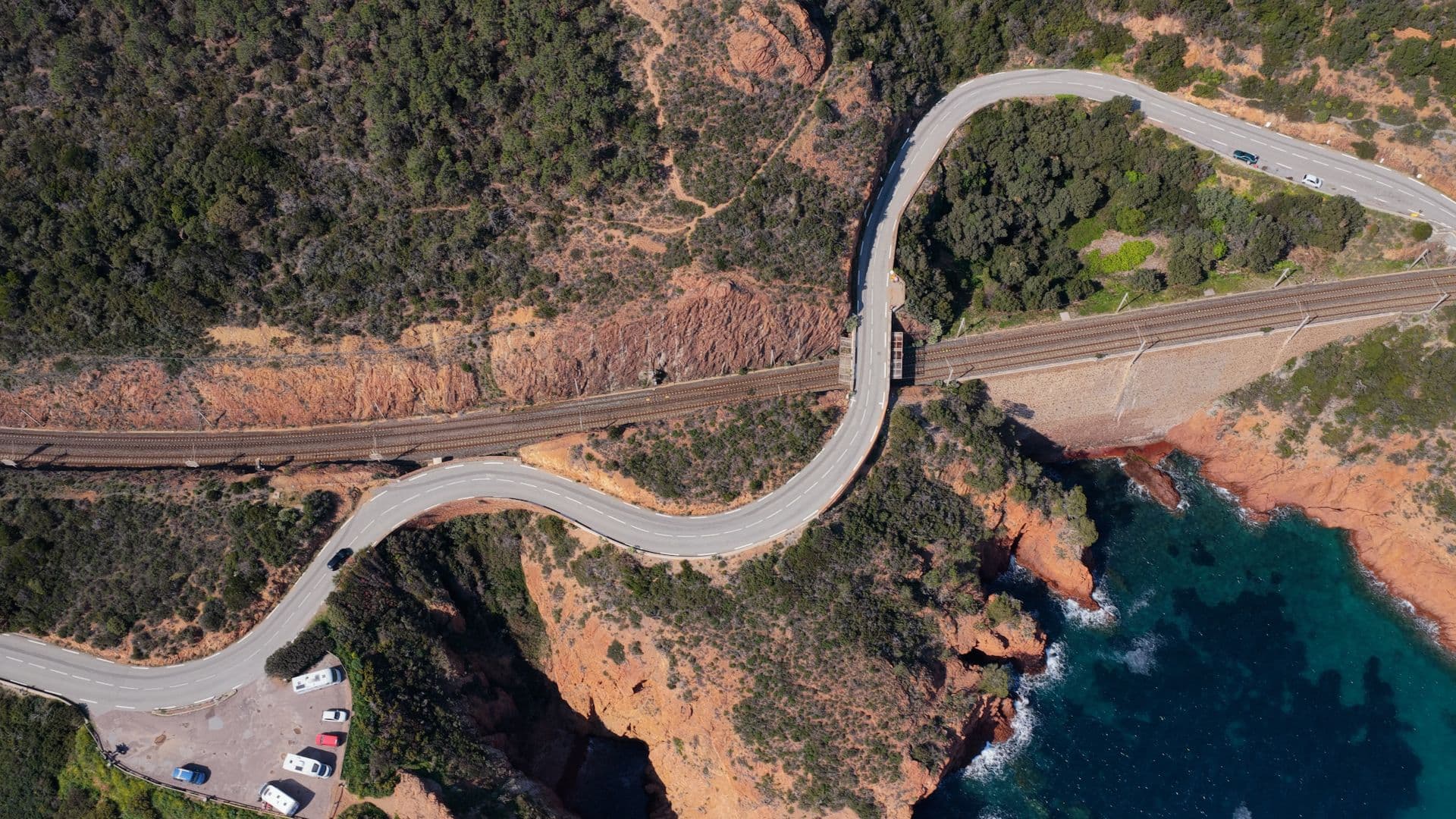 vue du ciel sur la route de la corniche de l'esterel et les couleurs rouge, vert et turquoise du massif qui tombe dans la mer méditerrannée.