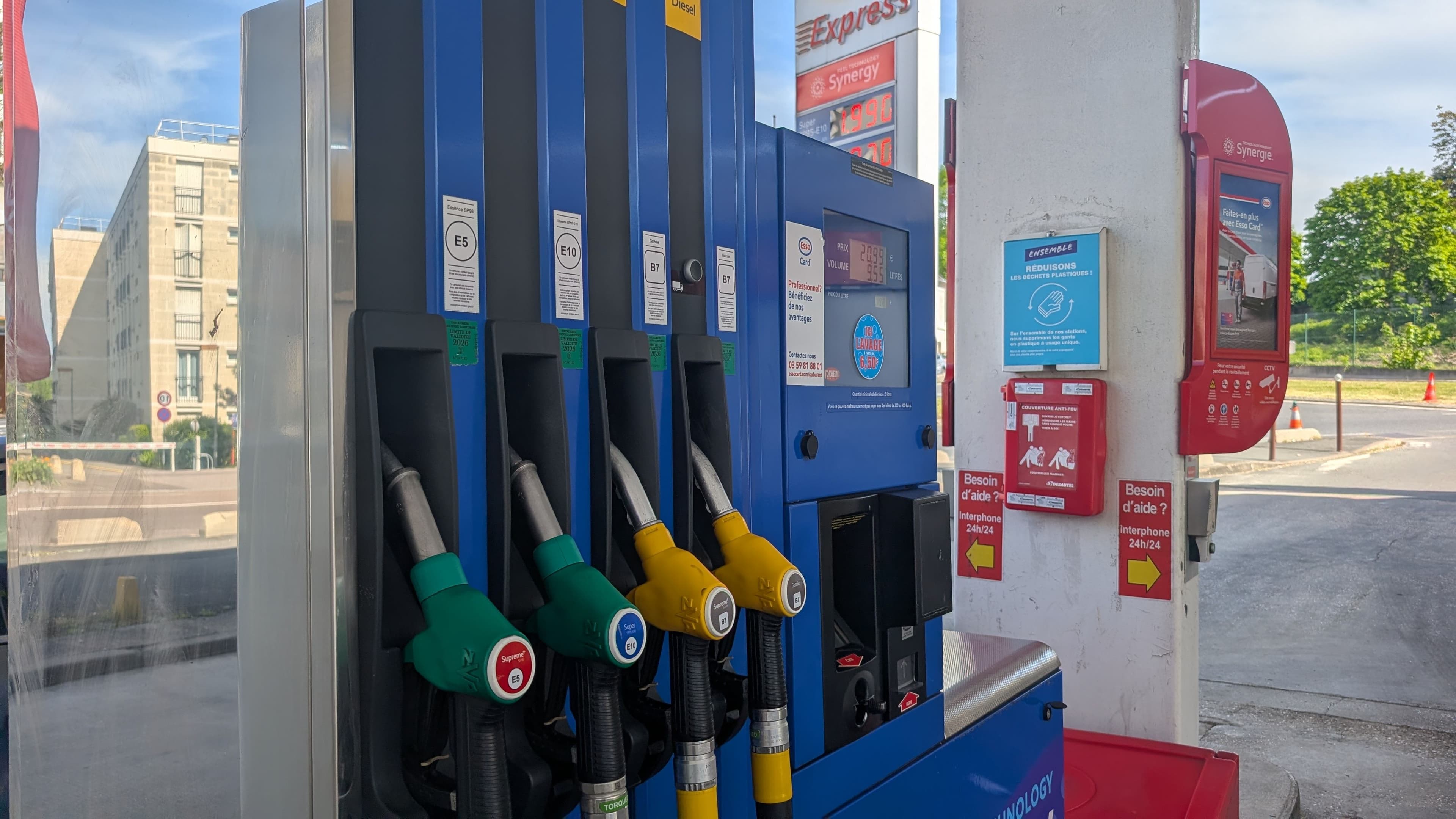 Une station essence Esso avec les pistolets des différents carburant et le totem affichant les tarifs en arrière plan