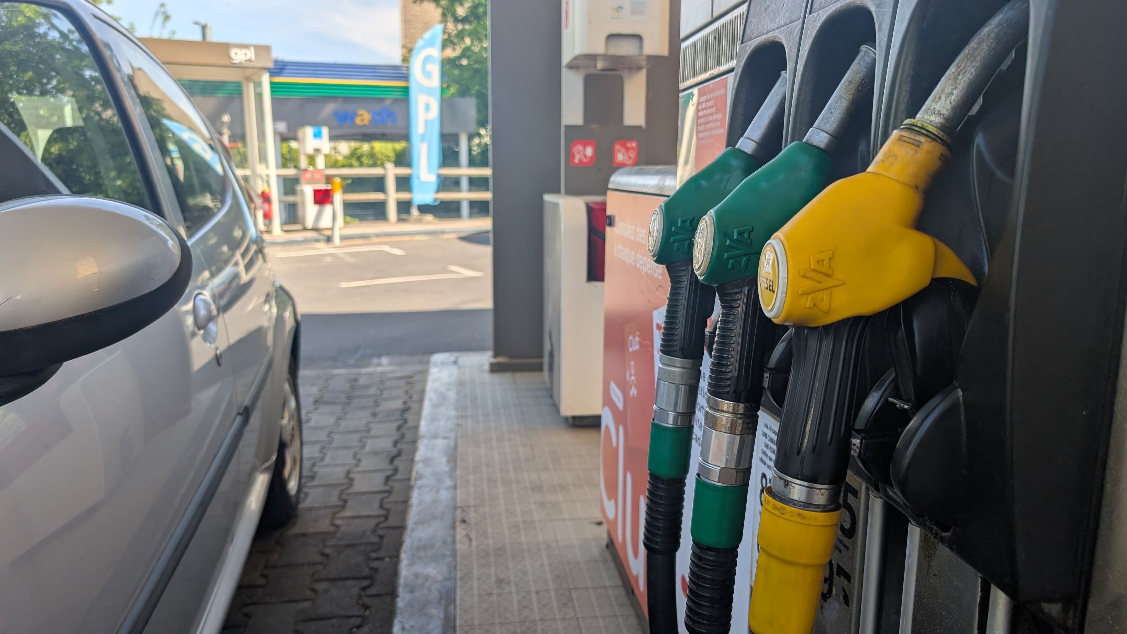 Zoom sur des pistolets de carburant à droite et le côté d'une voiture blanche à gauche.