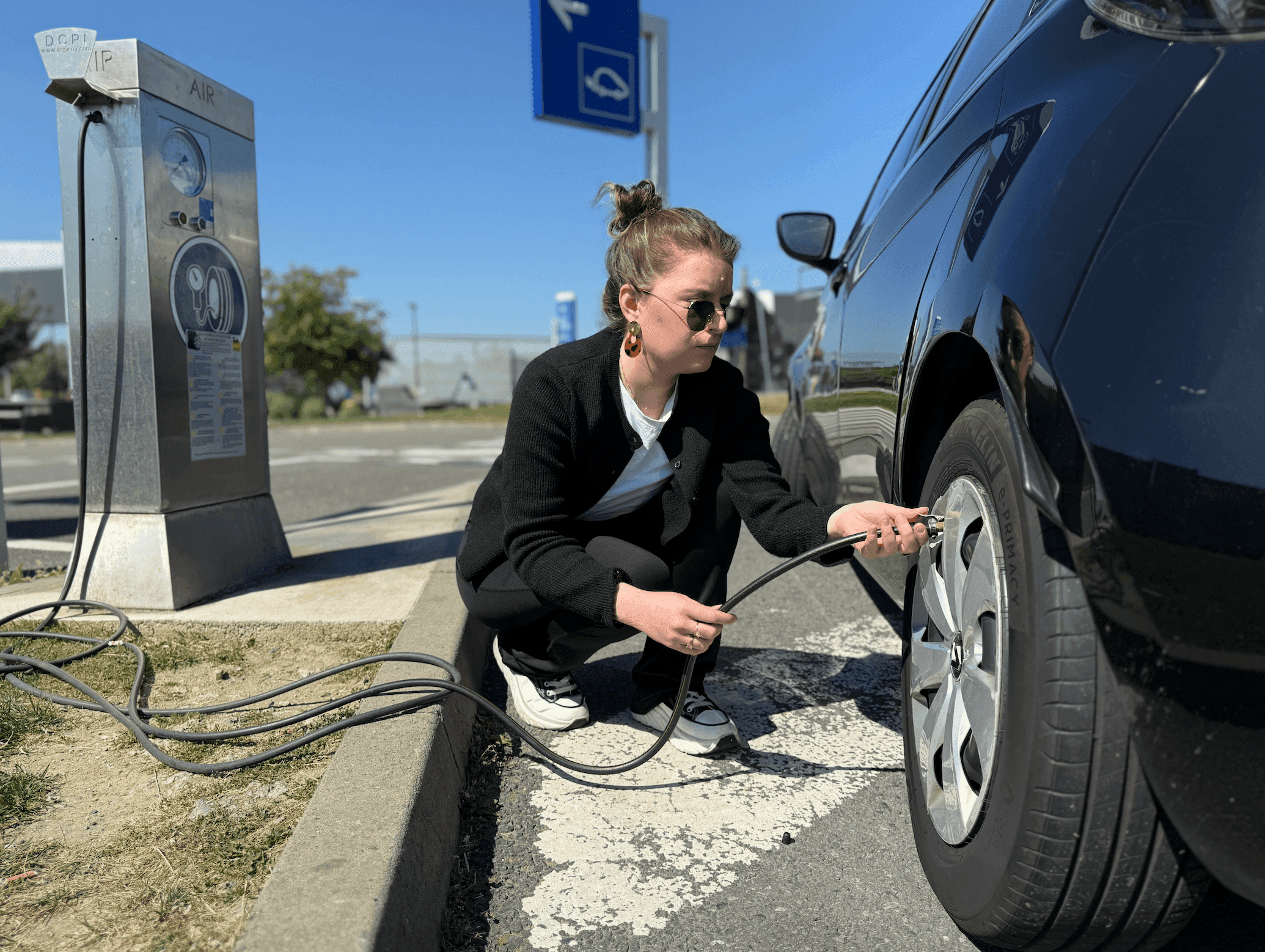 Une femme en train de faire la pression d'un pneumatique sur une aire d'autoroute.