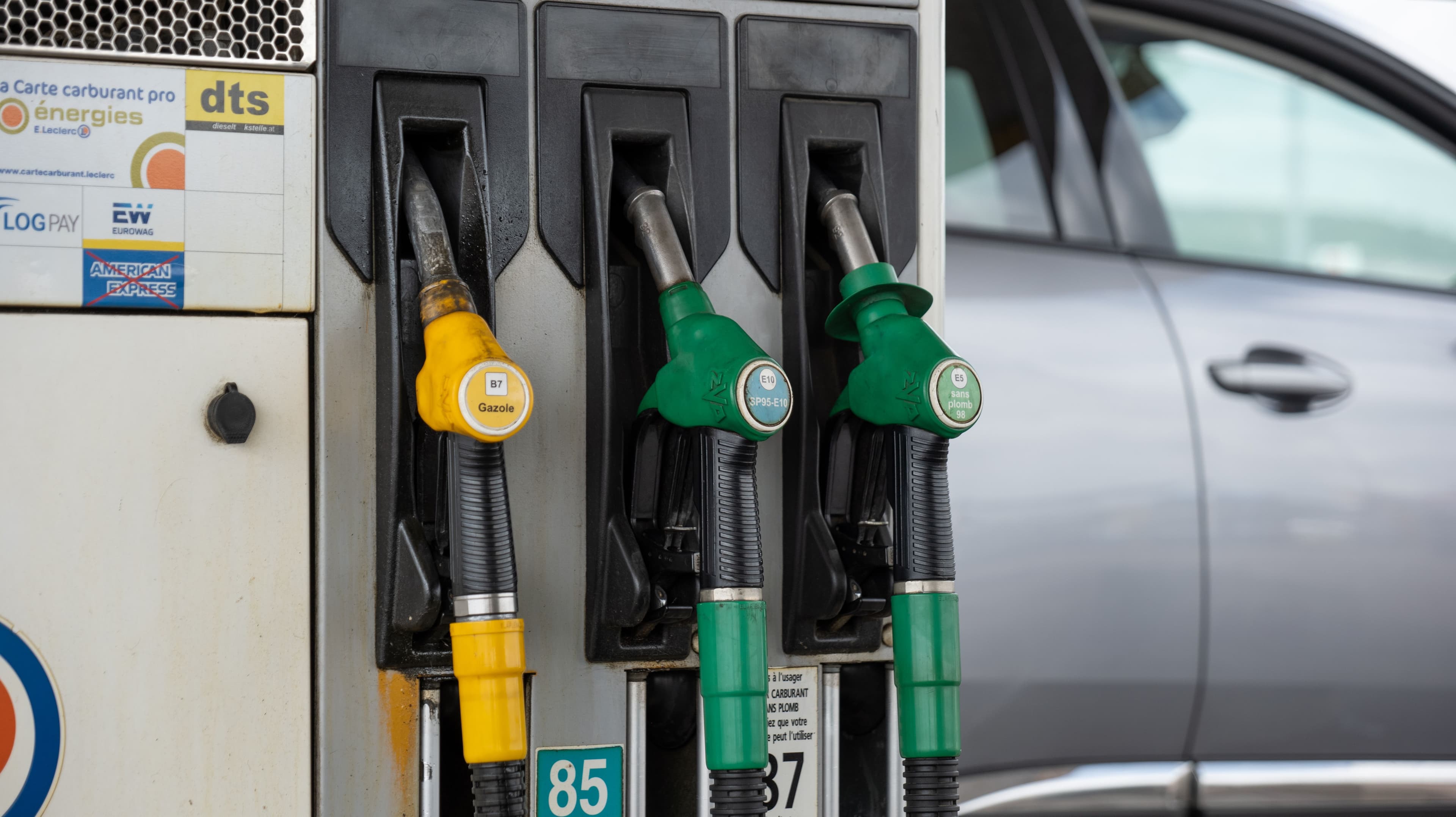 Des pistolets d'essence, SP95, SP98, gasoil, diesel dans un magasin E.Leclerc. Une voiture grise en fons.