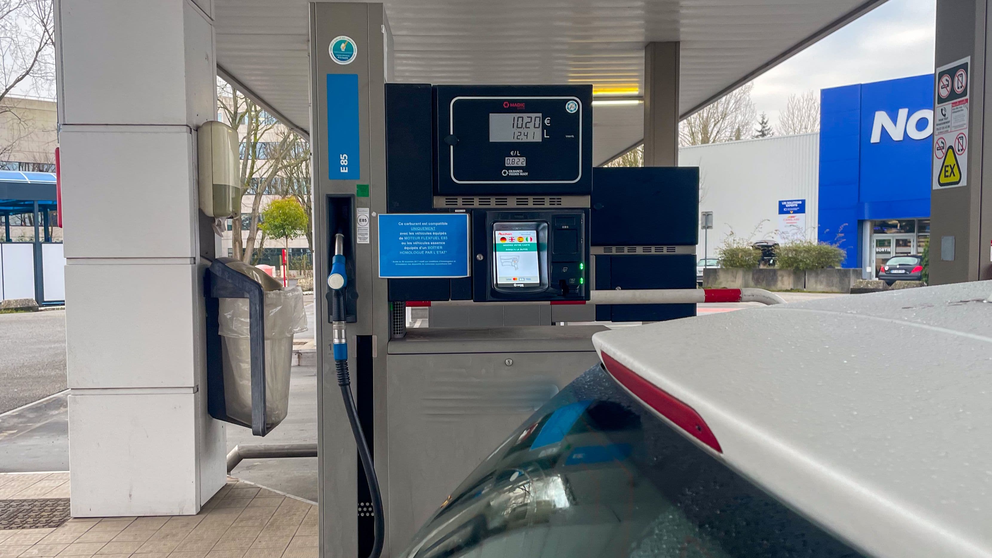Une pompe à superéthanol E85 dans une station-essence, une voiture blanche en premier plan.