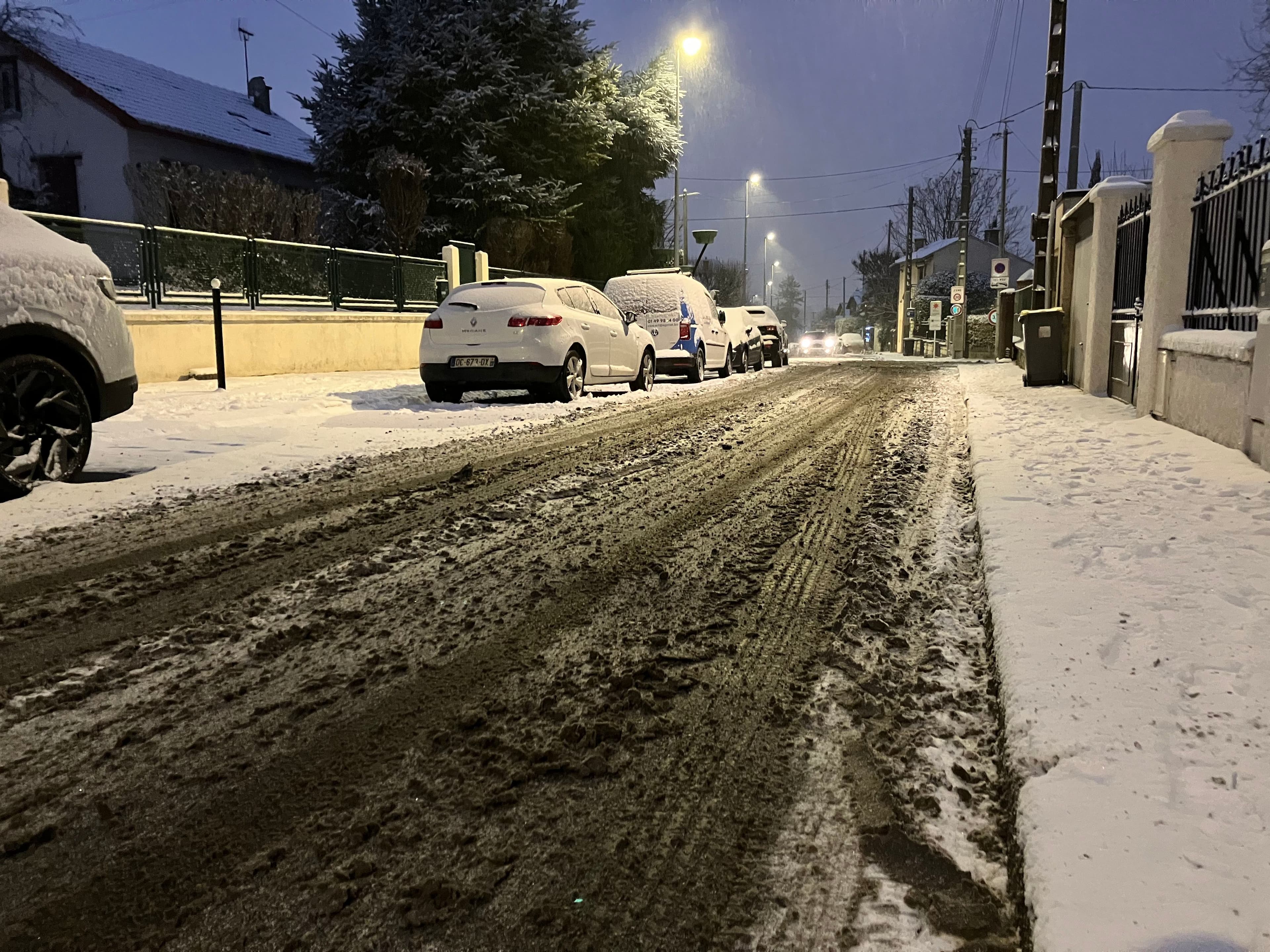 Une rue enneigée avec des voitures stationnée.