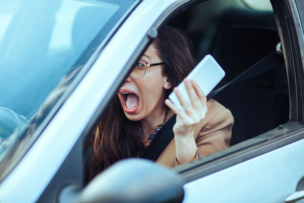 Une femme crie et tient son téléphone au volant.