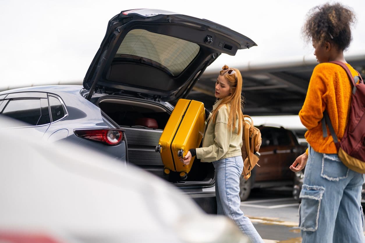 Une femme installe une valise dans le coffre de sa voiture.