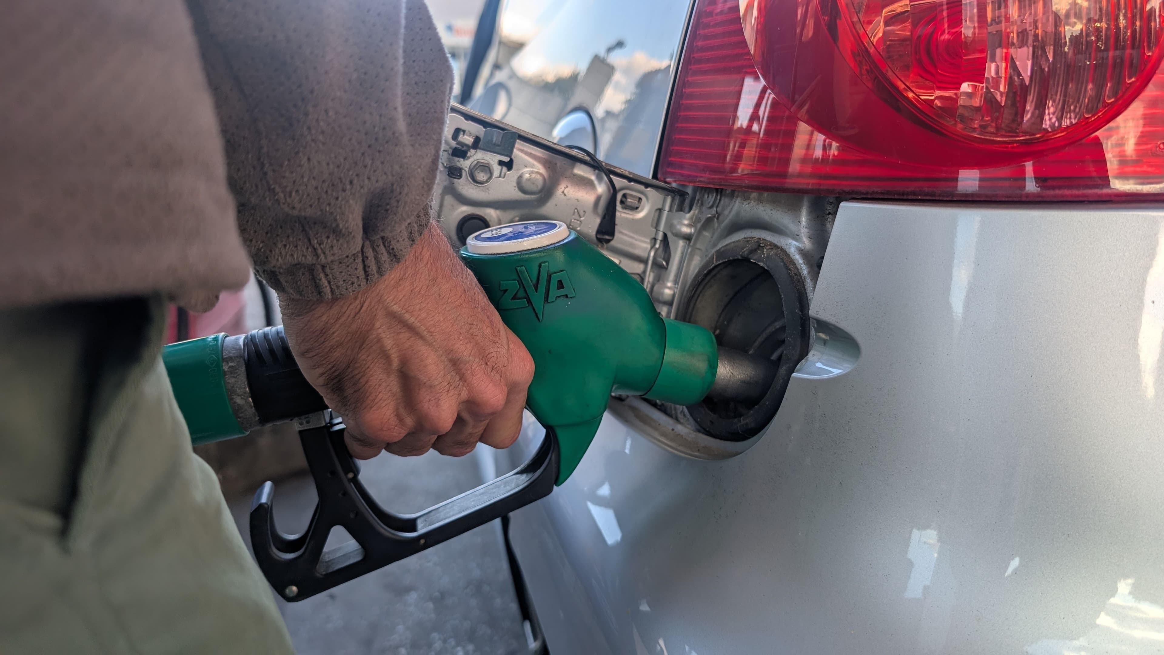 Un automobiliste fait le plein avec un pistolet vert de pompe à essence inséré dans une voiture grise.