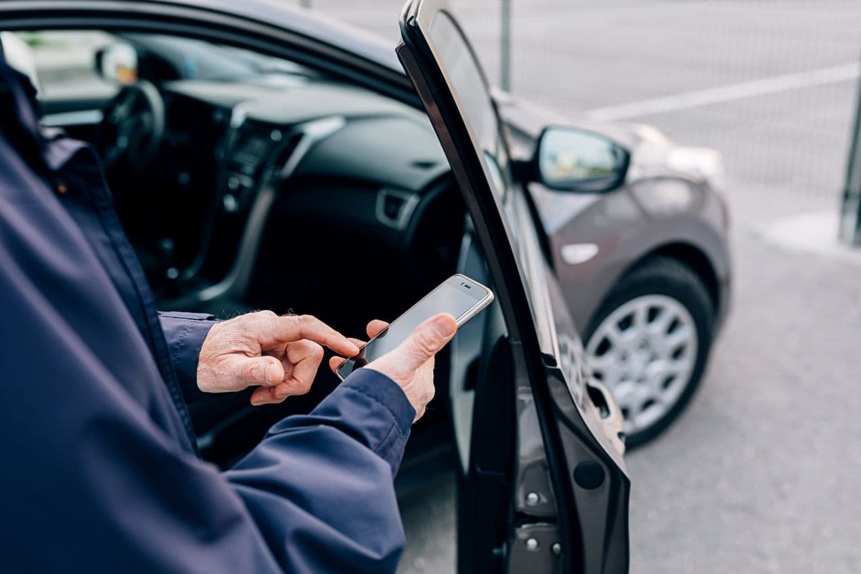 Personne utilisant un smartphone à côté d’une voiture ouverte