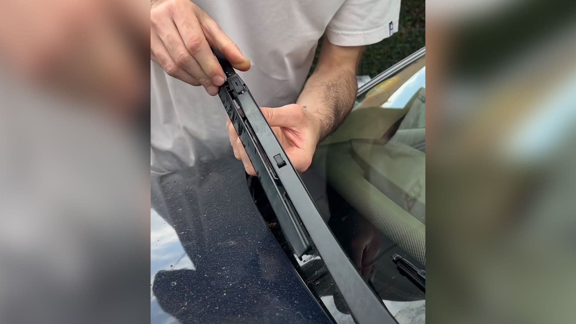 Un mécanicien remplace le balai d’essuie-glaces de sa voiture face caméra.