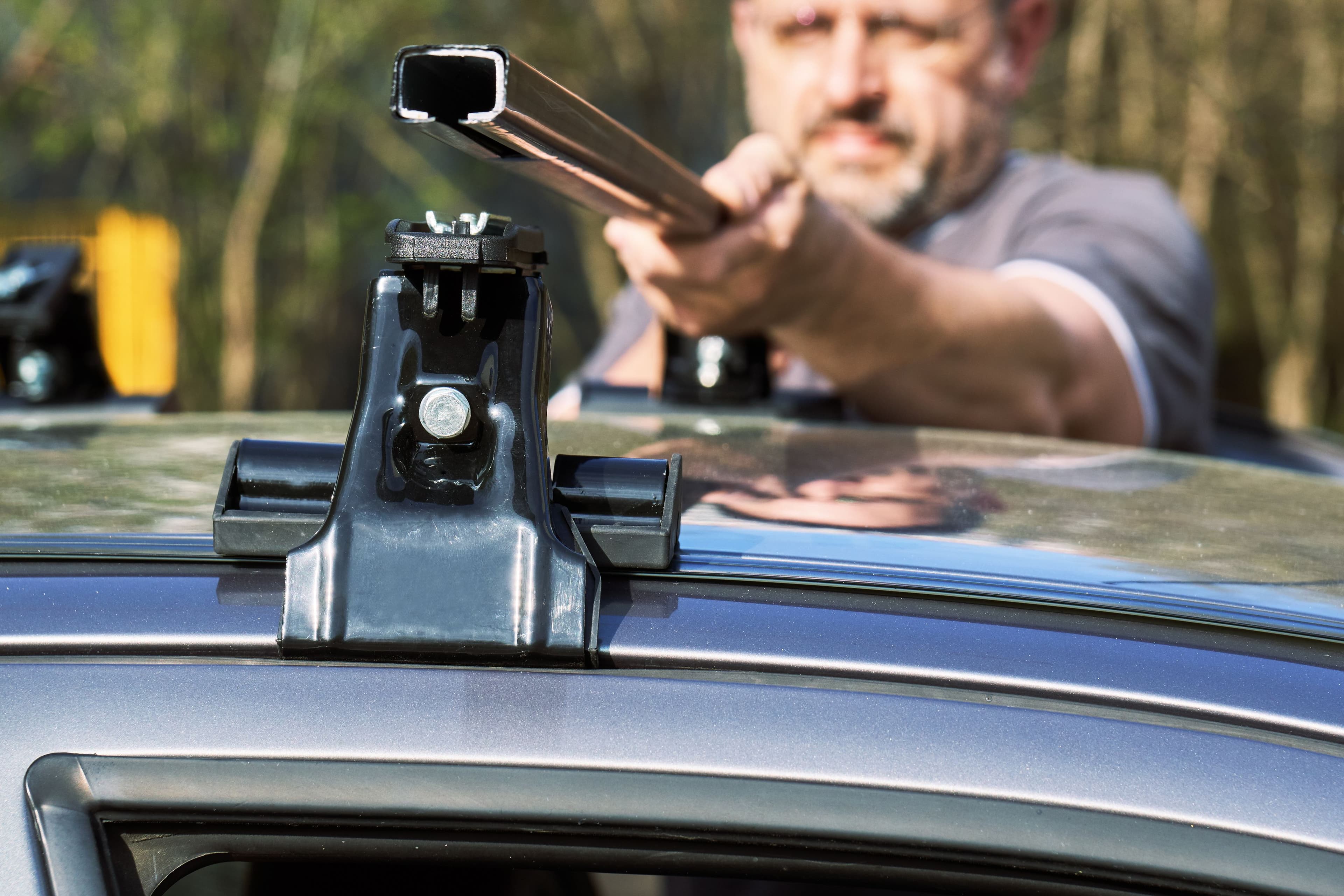Une photo d'un homme en train d'installer les barres de toit sur sa voiture pour représenter notre quiz sur les accessoires des véhicules