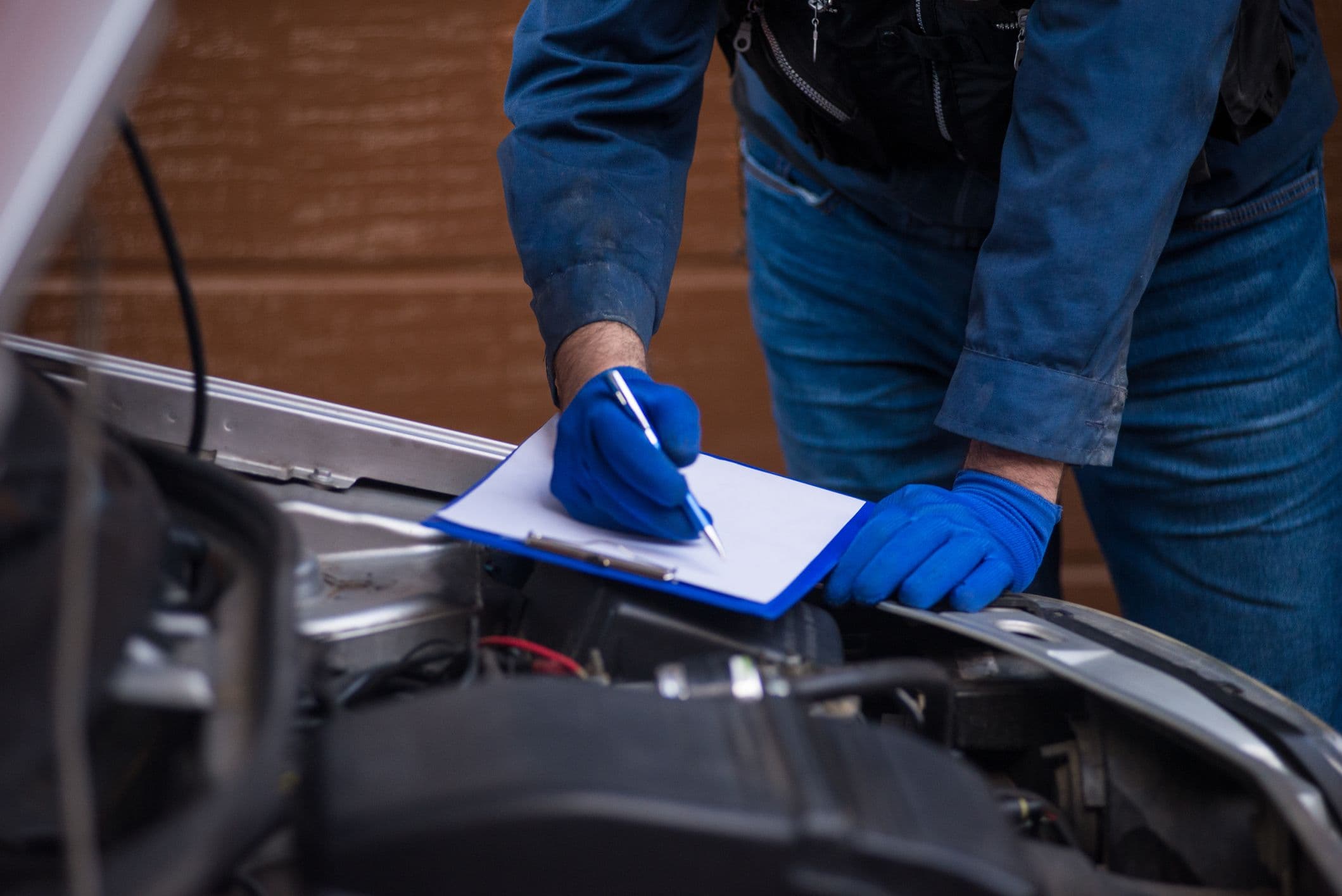 Un contrôleur remplit les informations du contrôle technique sur le capot ouvert d'une voiture