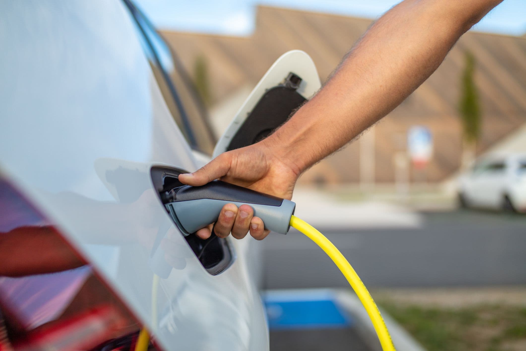 La main d'un homme tient un cable de recharge, branché sur une voiture électrique blanche