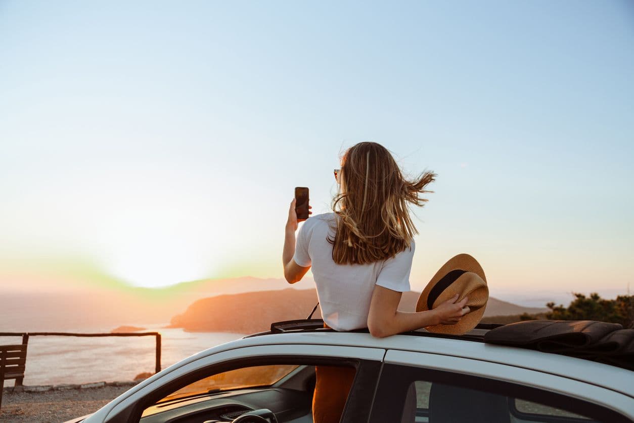 une femme prend une photo d'un coucher de soleil depuis sa voiture garée