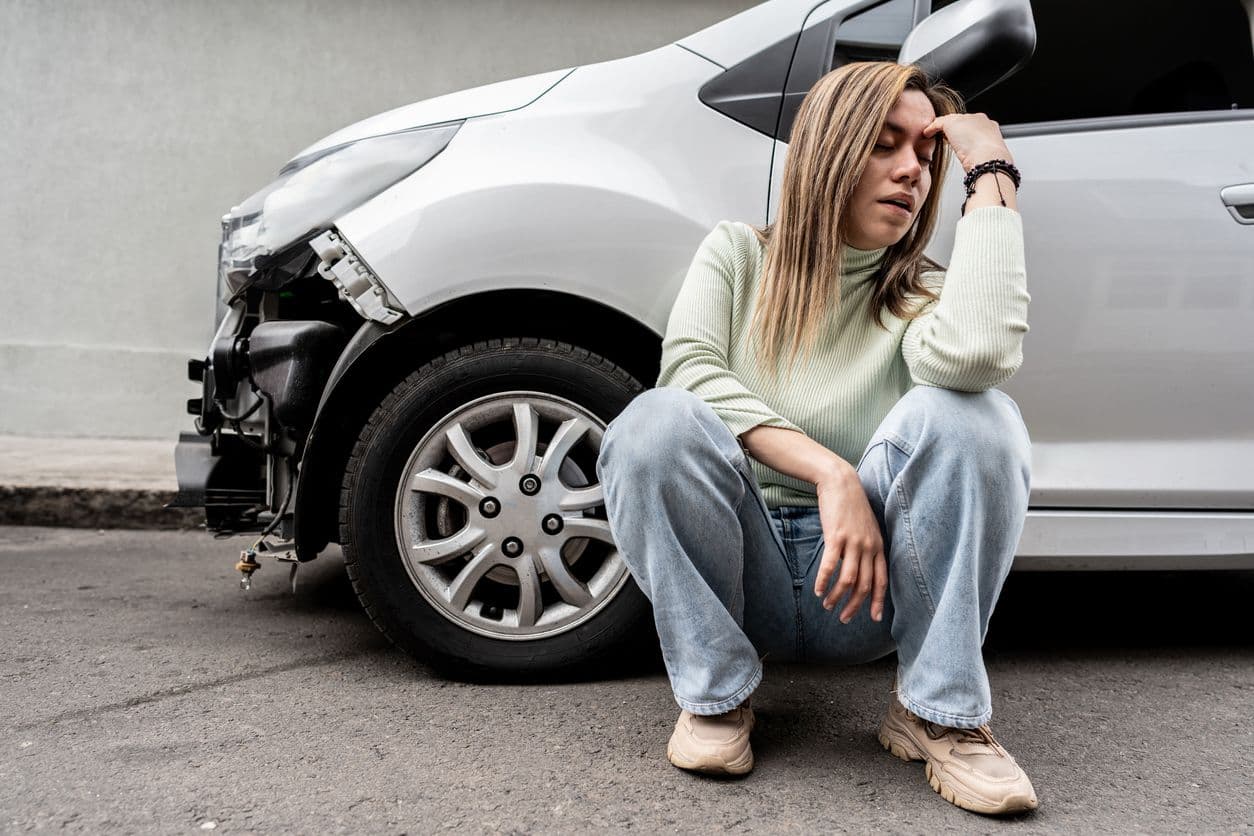 Femme assise à côté d'une voiture abîmée après un accident.