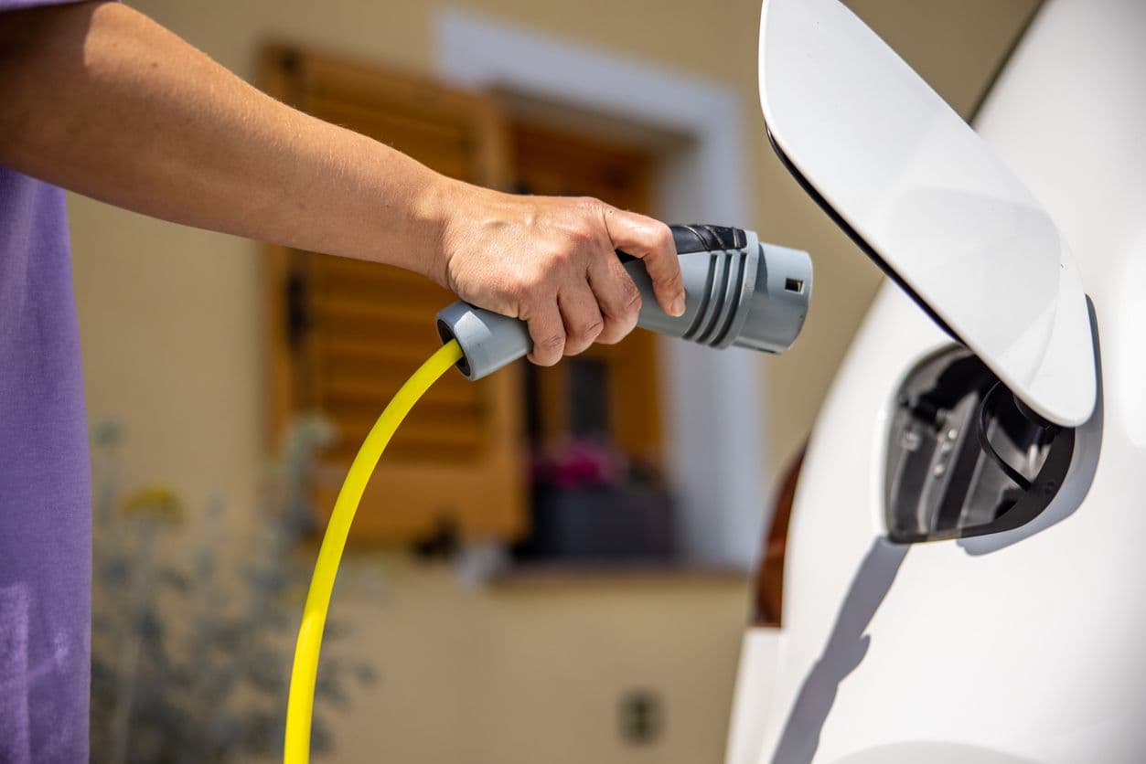 Quelqu'un branche sa voiture électrique blanche devant sa maison