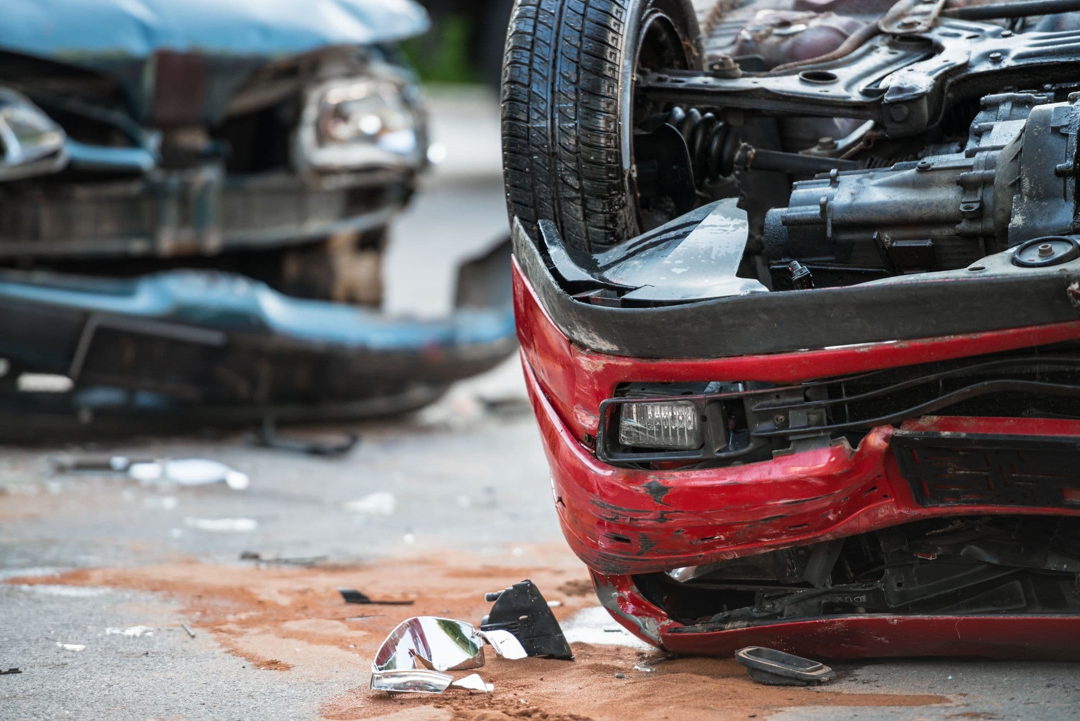 Deux voitures accidentées : une voiture rouge retournée au premier plan, une voiture bleue cabossée en arrière-plan
