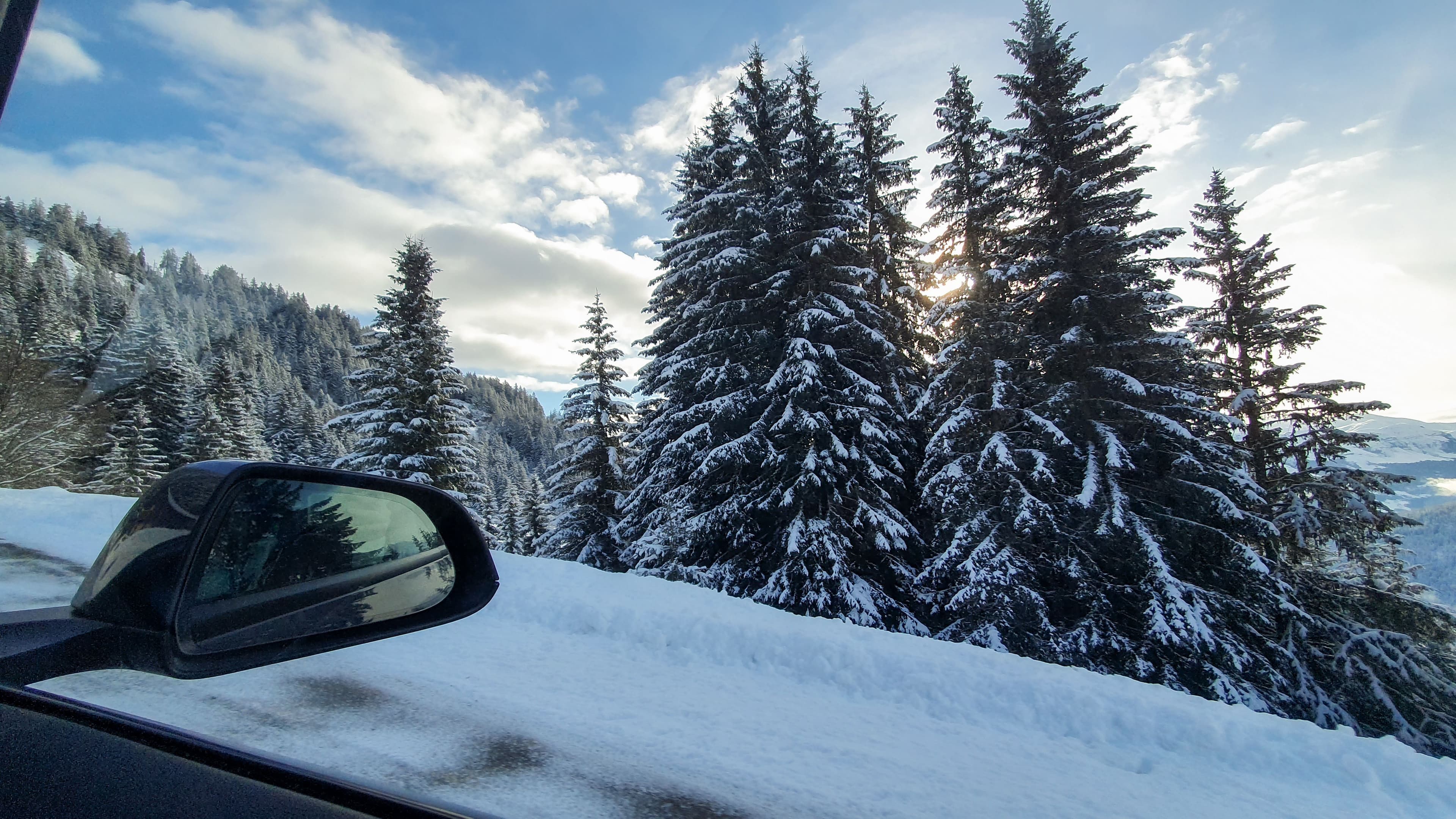 une route de montagne enneigée prise de l'intérieur d'une voiture, avec reflet dans le rétroviseur