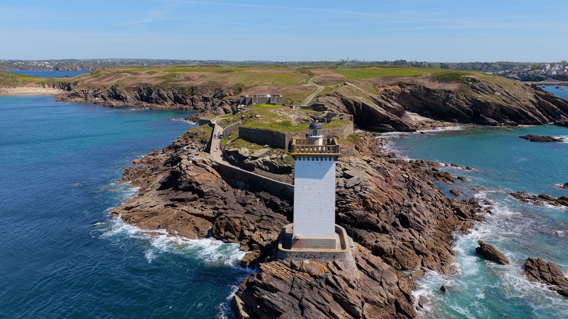 Un phare blanc solitaire sur une côte rocheuse avec une mer bleue.