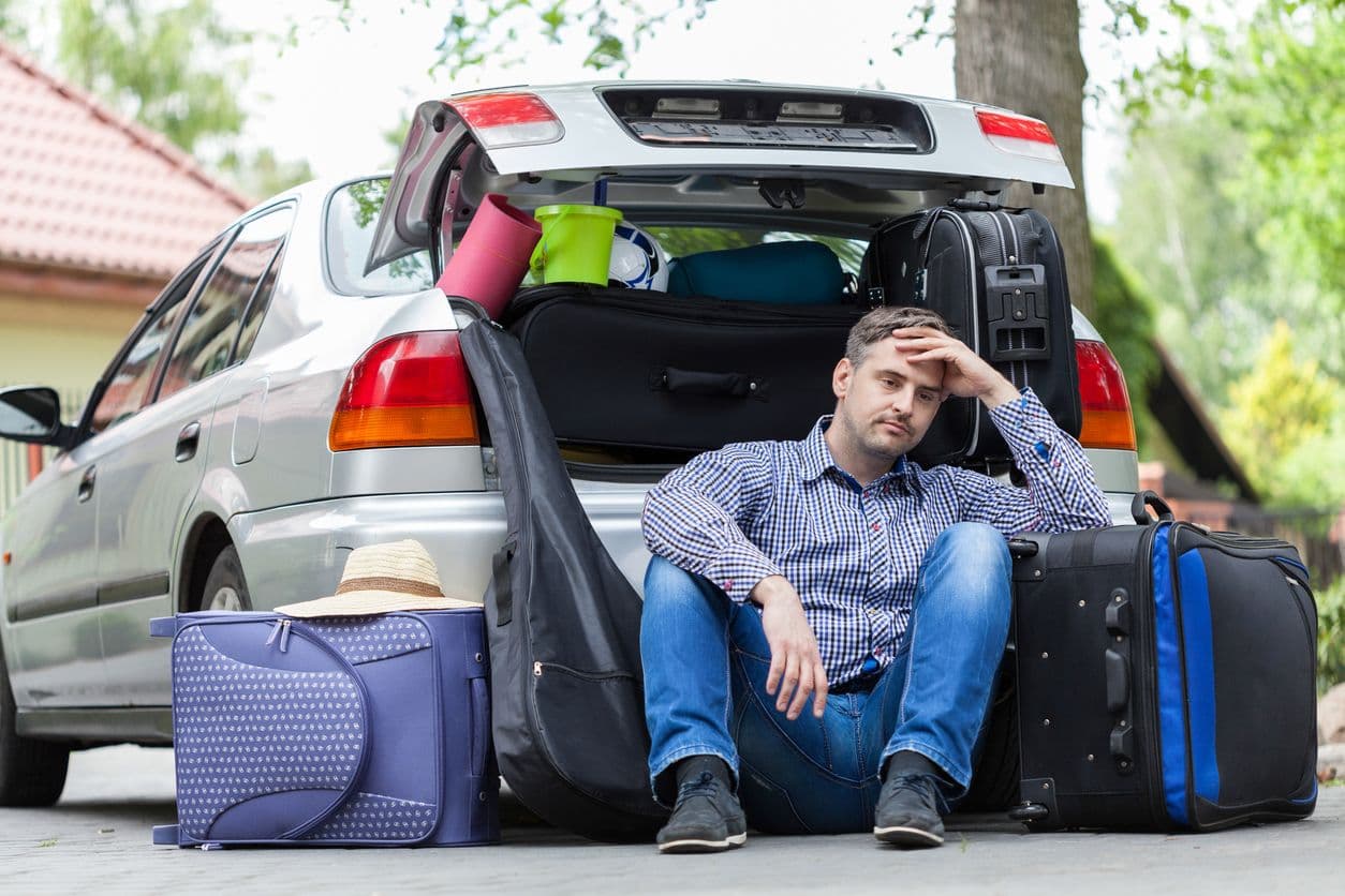 Un homme tente de faire entrer tous ses bagages dans le coffre de sa voiture
