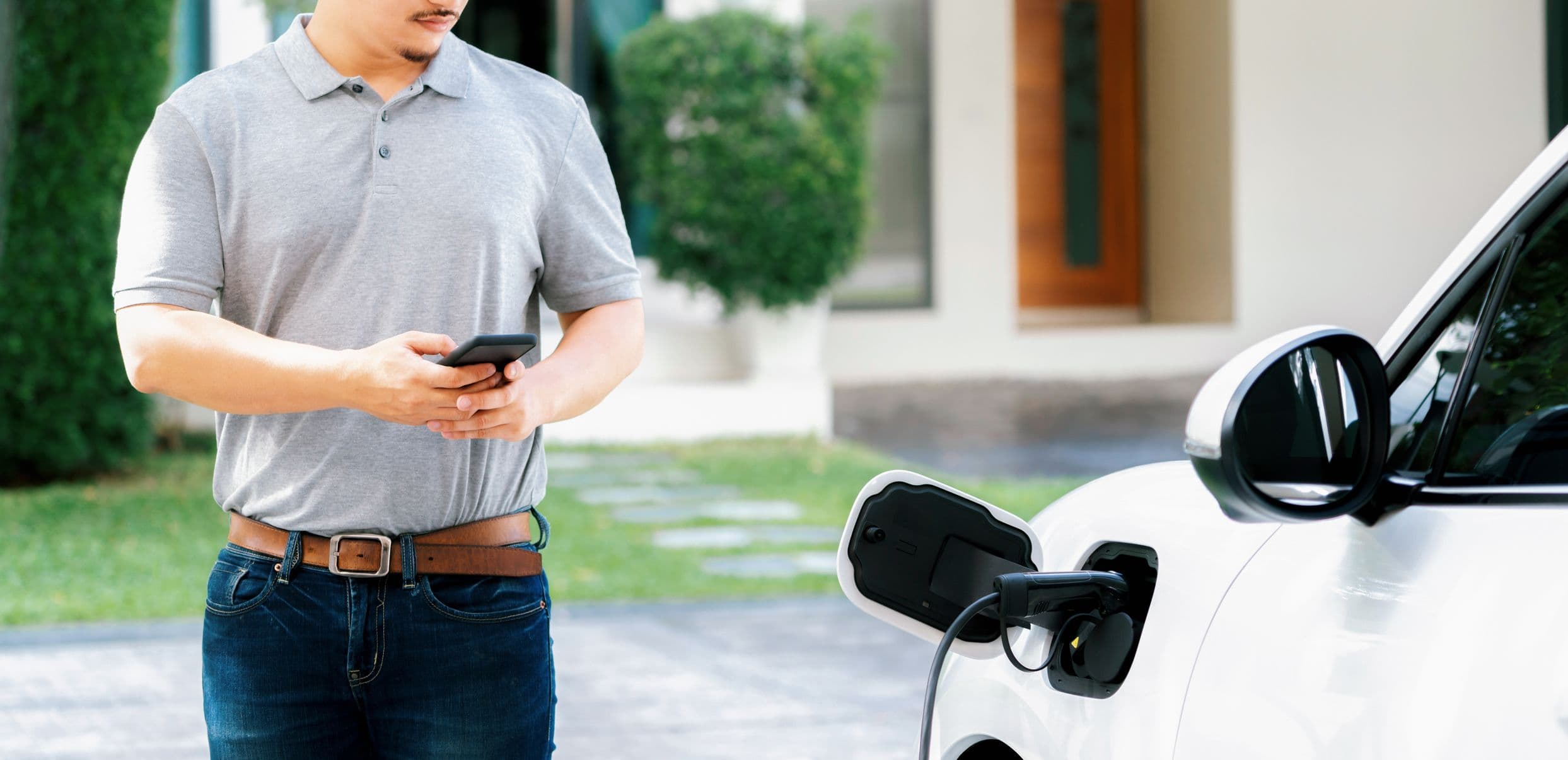 Un homme sur son smartphone pendant la recharge de sa voiture électrique