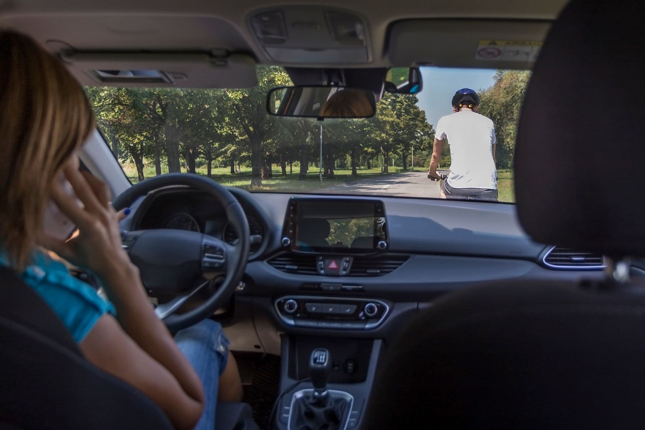 Conductrice au volant utilisant son téléphone portable, risquant de percuter un cycliste sur la route.