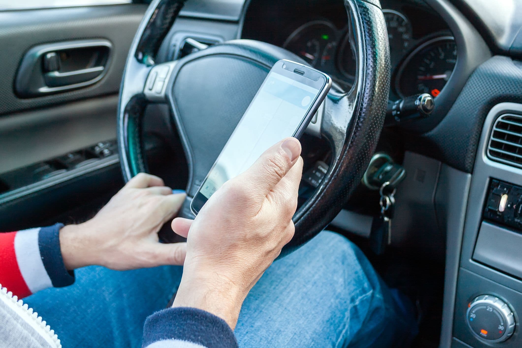 Un homme au volant de sa voiture tient en main son téléphone 