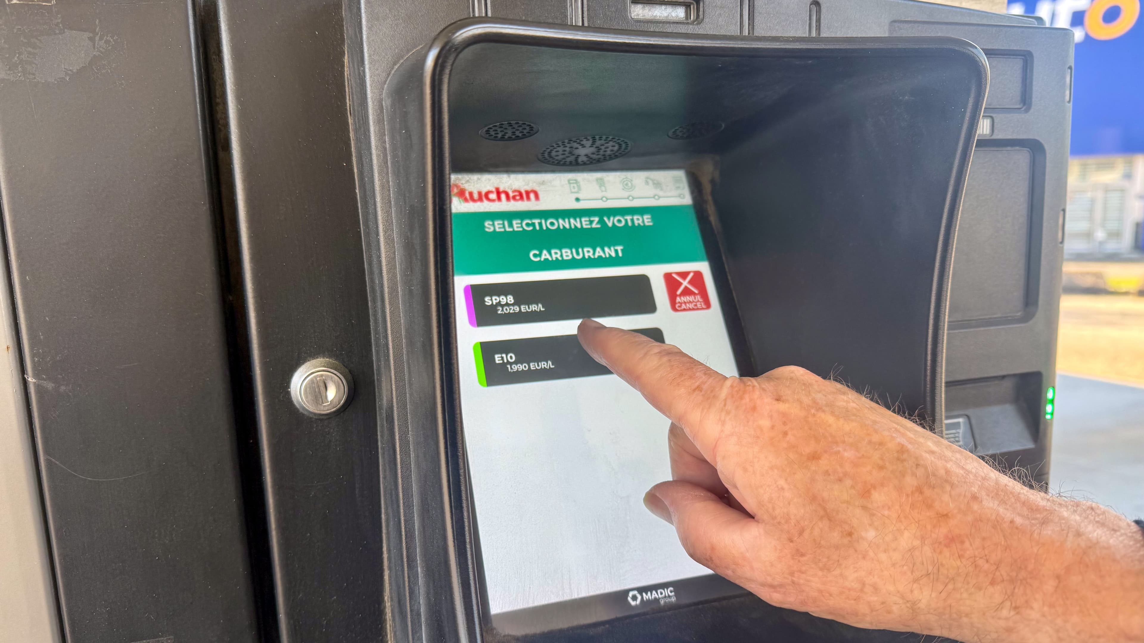 Un homme sélectionne du carburant SP98 sur un écran tactile de borne Auchan