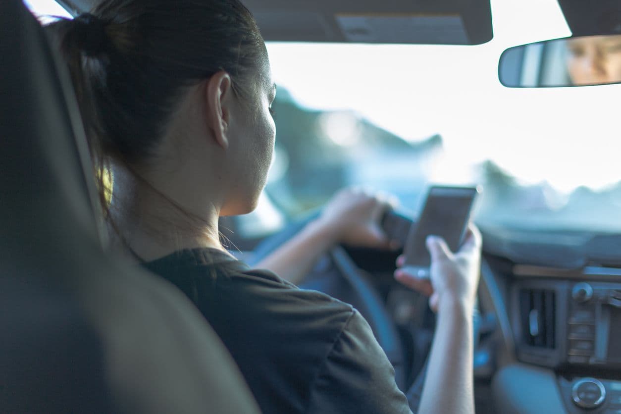 une femme tient et regarde son téléphone, tout en étant au volant de sa voiture