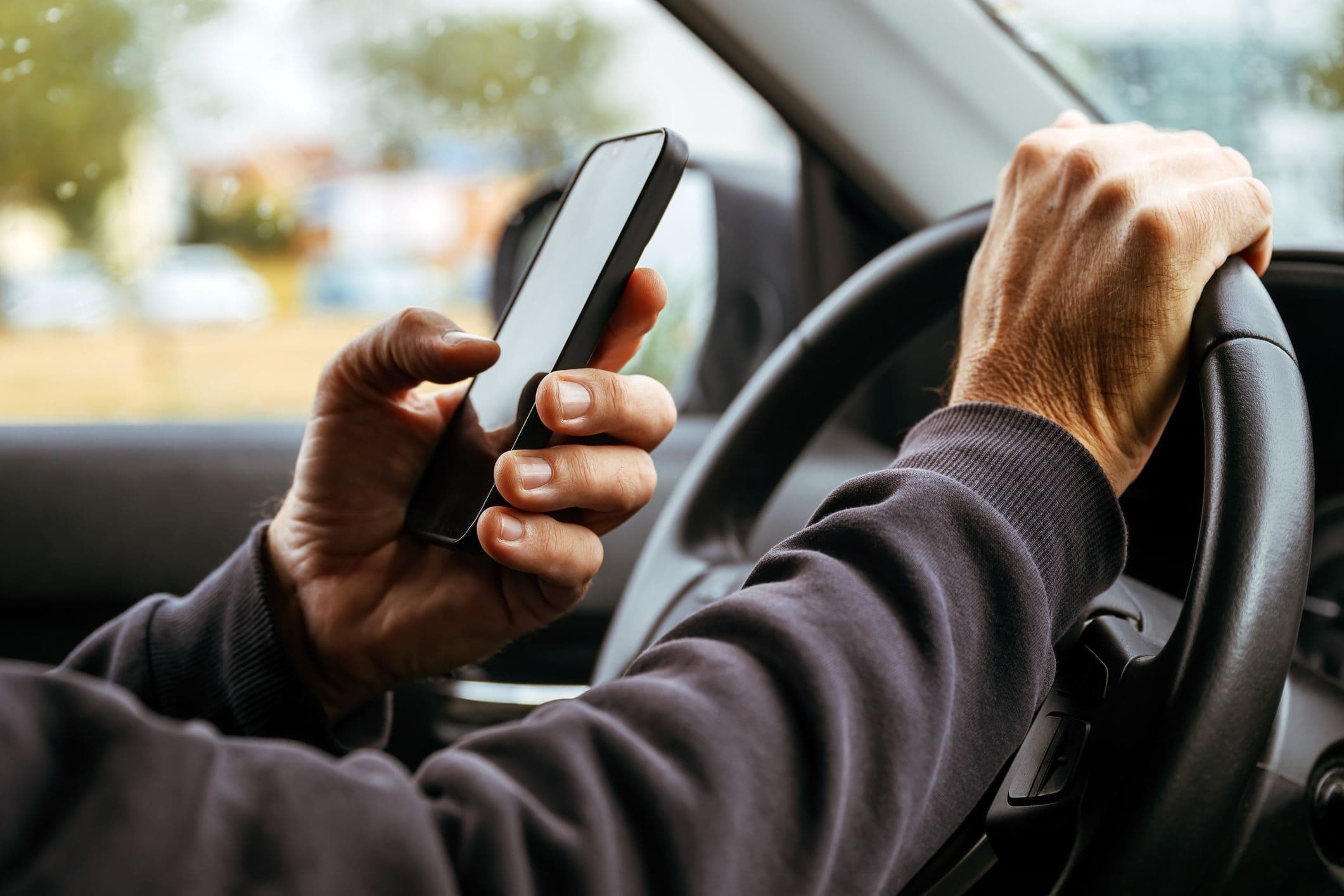 Conducteur tenant un smartphone en conduisant, main sur le volant