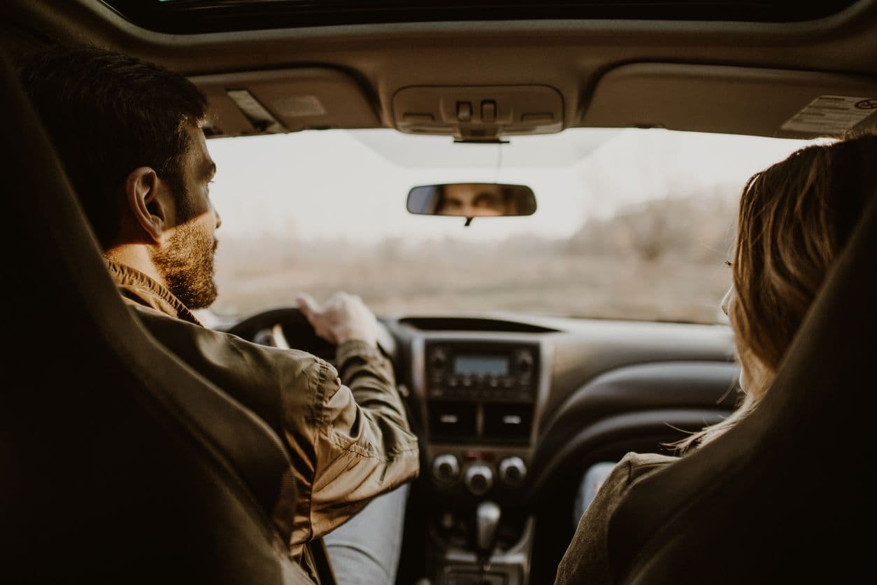 un couple en voiture, l'homme est au volant, les deux sont vus depuis la banquette arrière.