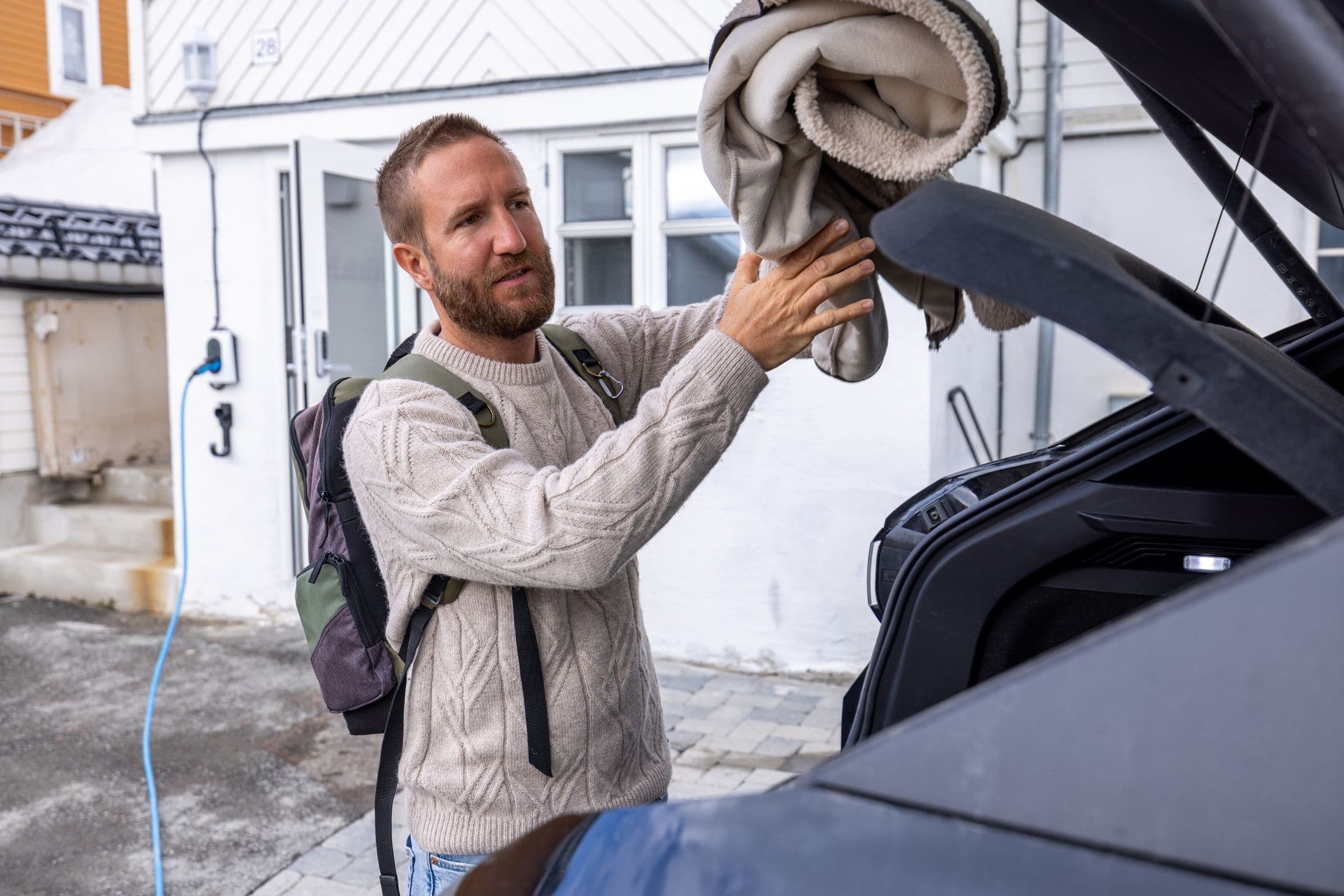 Homme inspectant le coffre ouvert d’une voiture électrique devant une maison