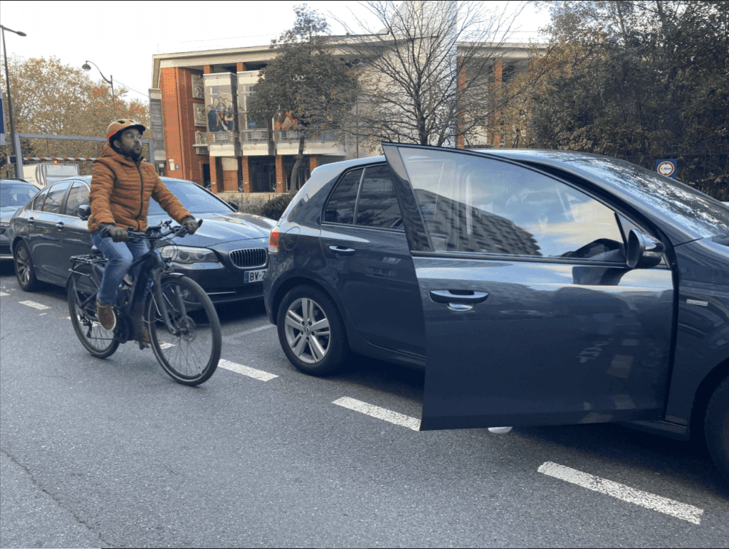 un passager de voiture ouvre sa portière sans voir arriver un cycliste dans son dos