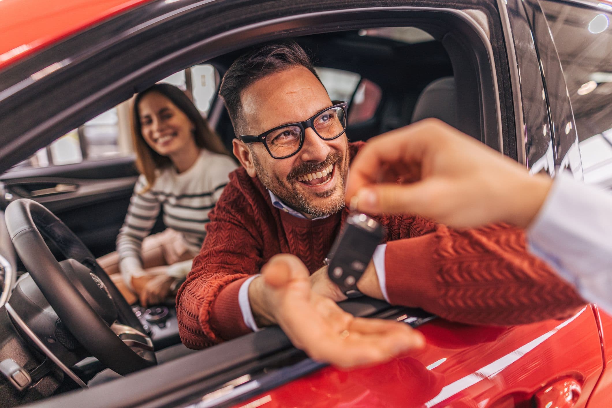 Un couple d'acheteurs recevant les clefs de leur nouvelle voiture par le vendeur.