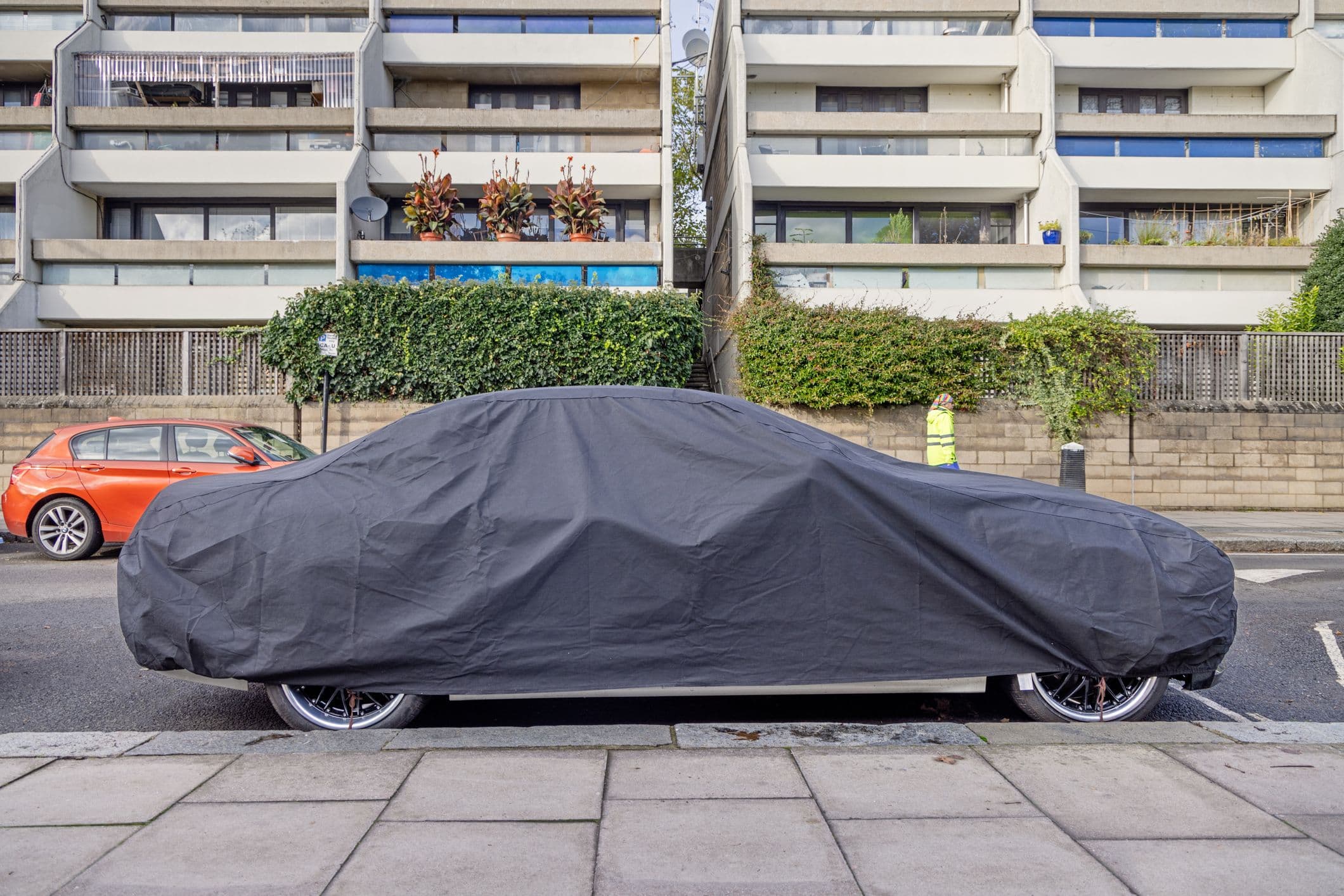 une voiture sous une bâche noire, stationnée dans la rue