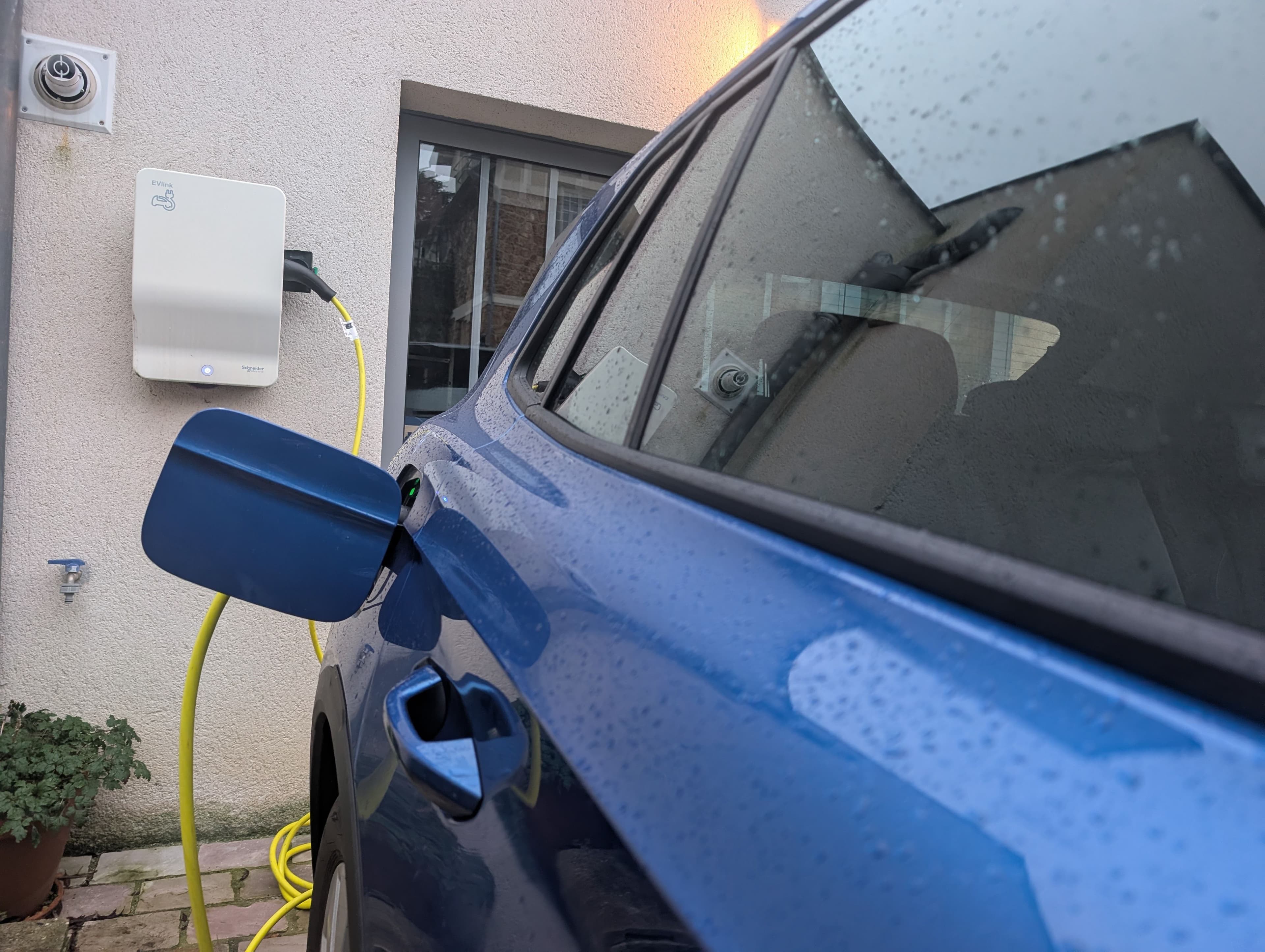 Une voiture électrique bleue en charge devant une maison de particulier