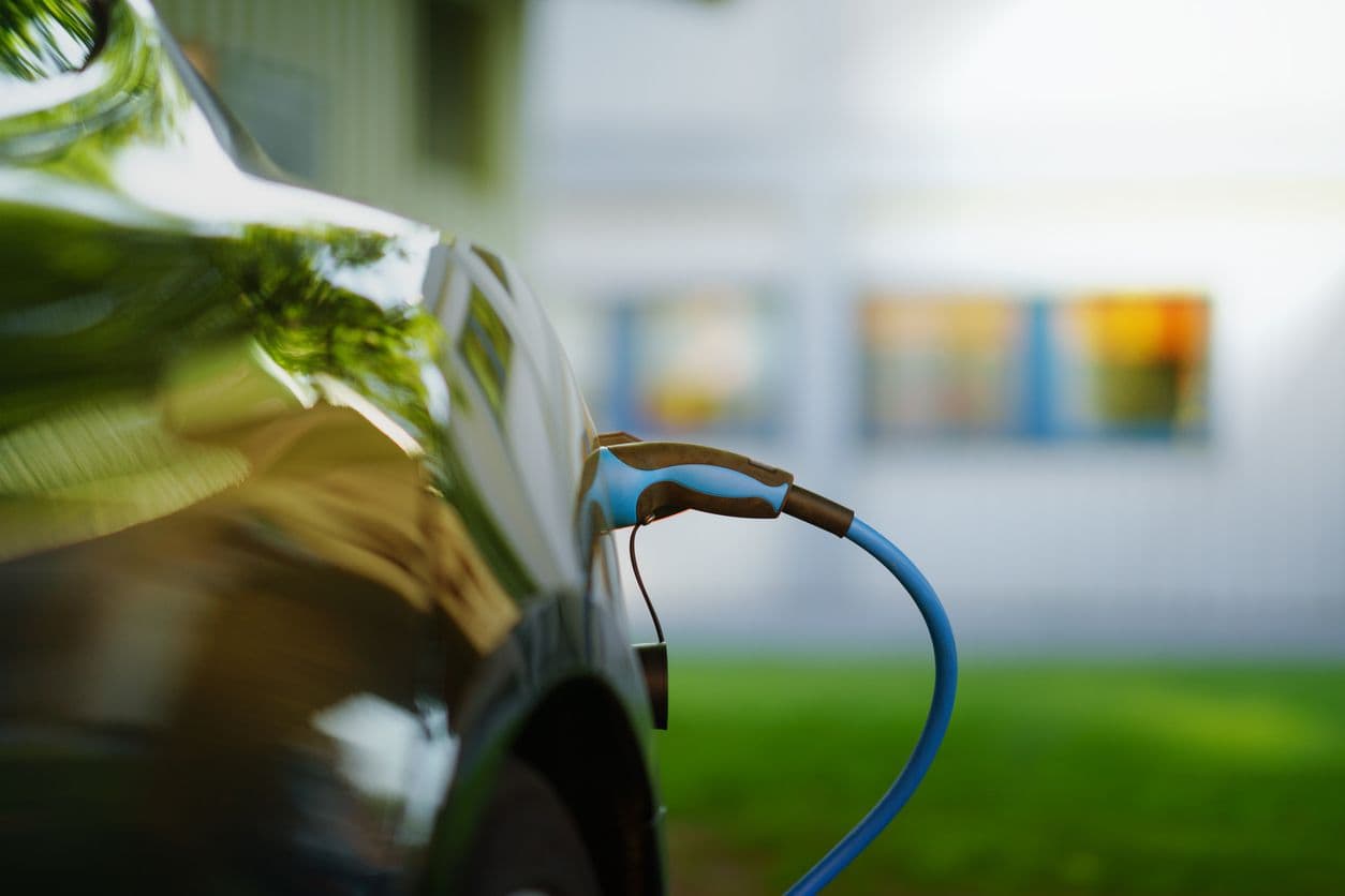 une voiture électrique en train de se recharger face à une maison