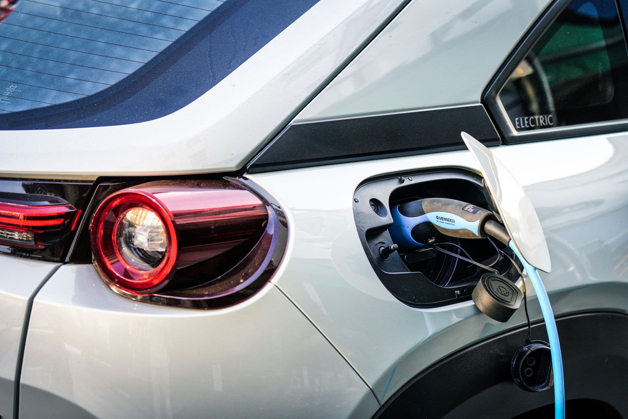 Une voiture électrique en train de se recharger. Zoom sur la trappe ouverte et le câbe de recharge branché.