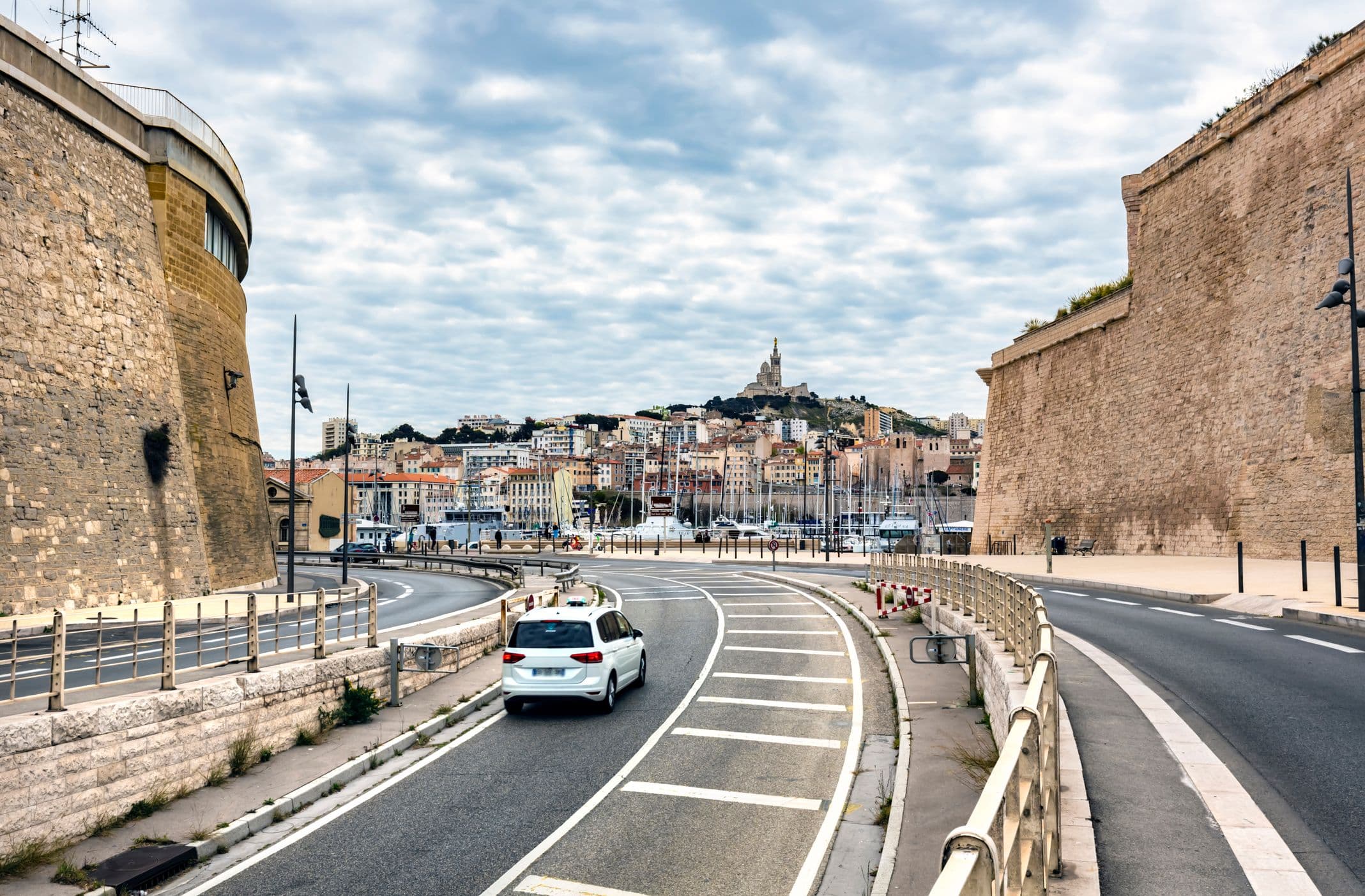 Une voiture blanche circule à Marseille, vue sur Notre Dame de la Garde