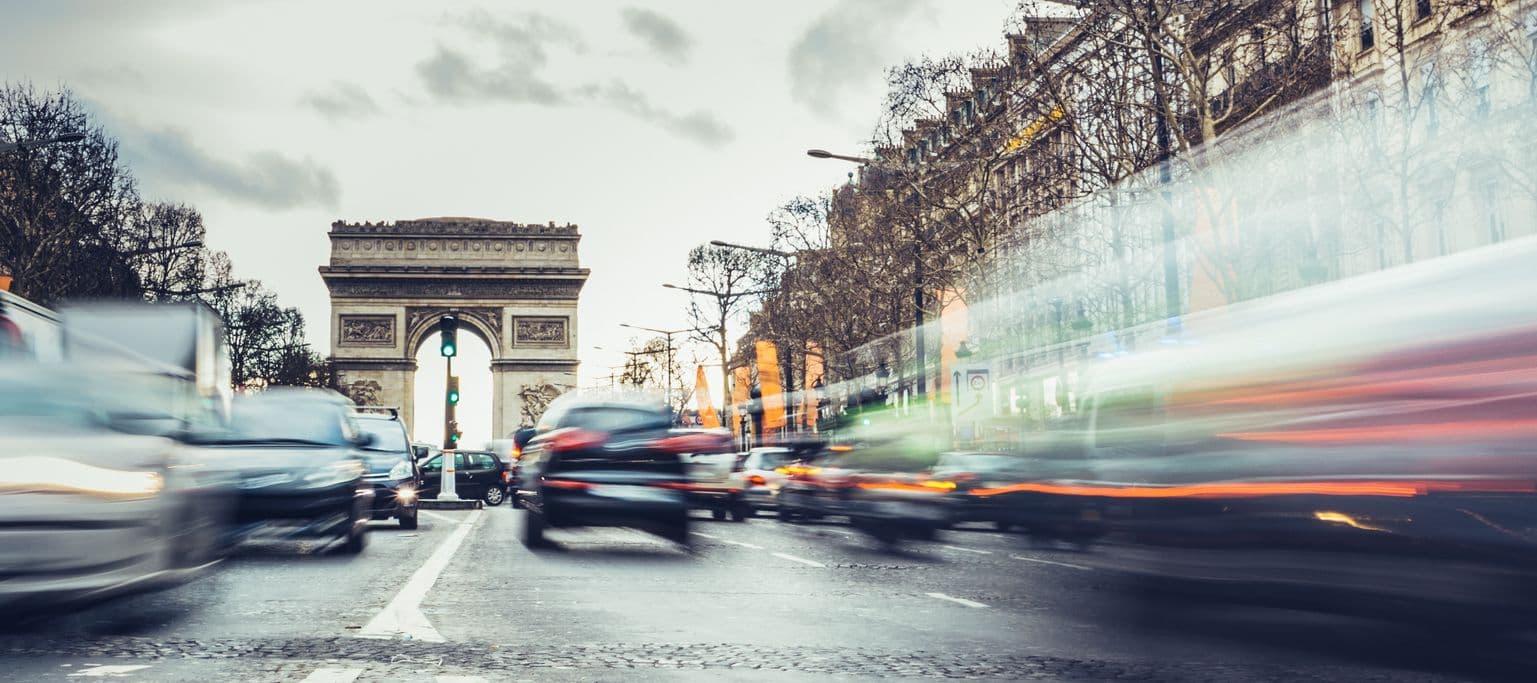 Des voitures roulent sur les champs élysées, avec l'arc de triomphe en fond