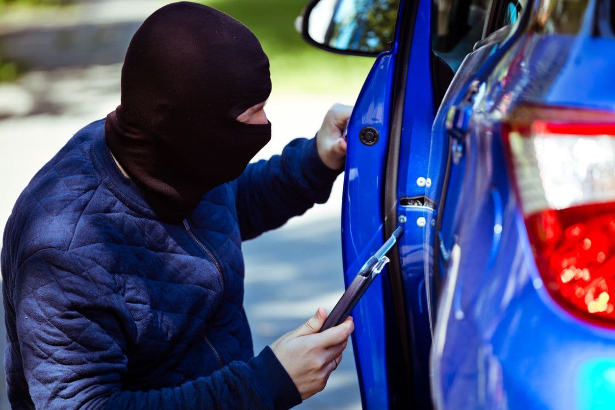 Un malfrat cagoulé vole une voiture grâce à une technique électronique et une tablette.