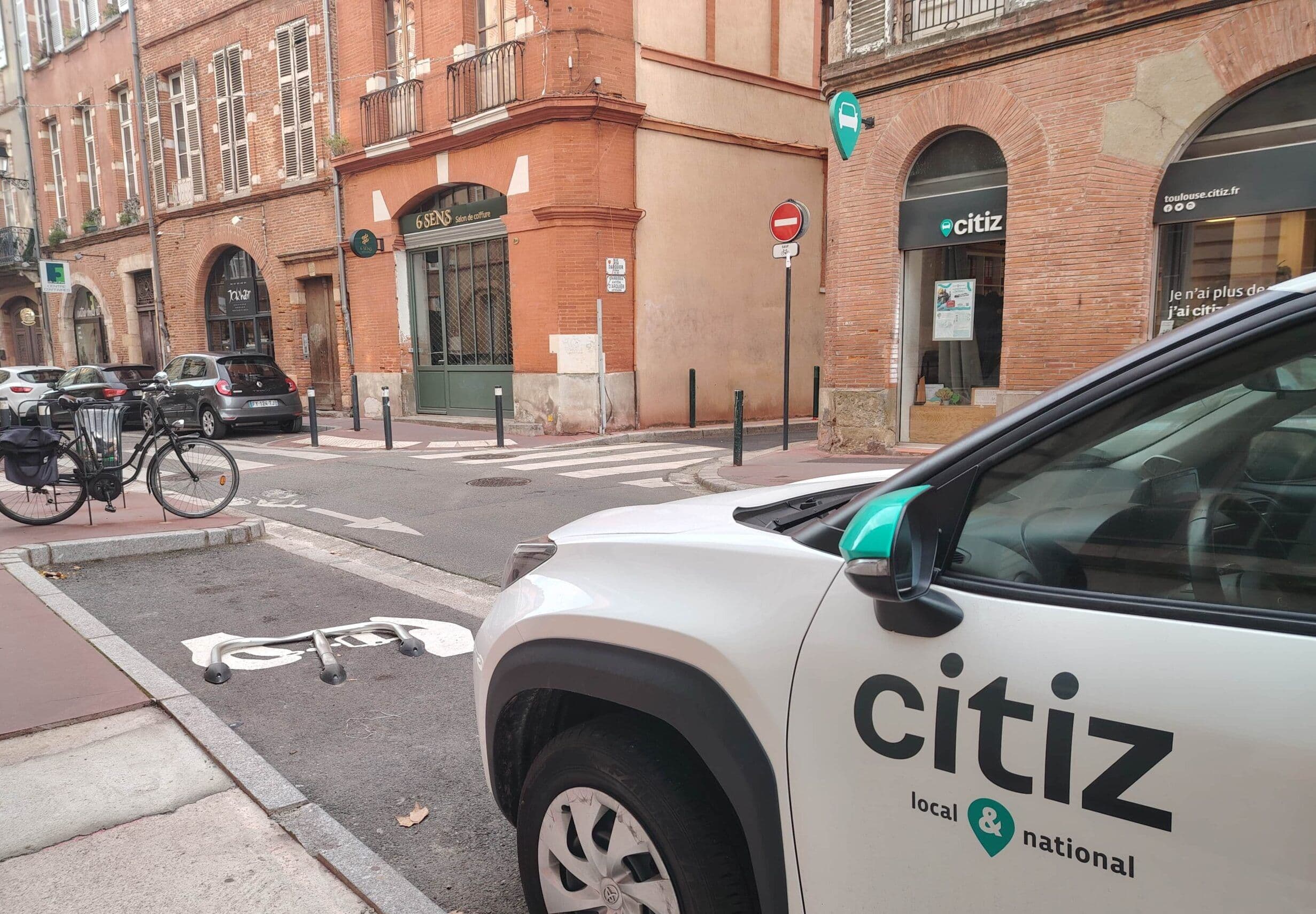 Voiture Citiz en premier plan devant une rue de Toulouse avec enseignes visibles