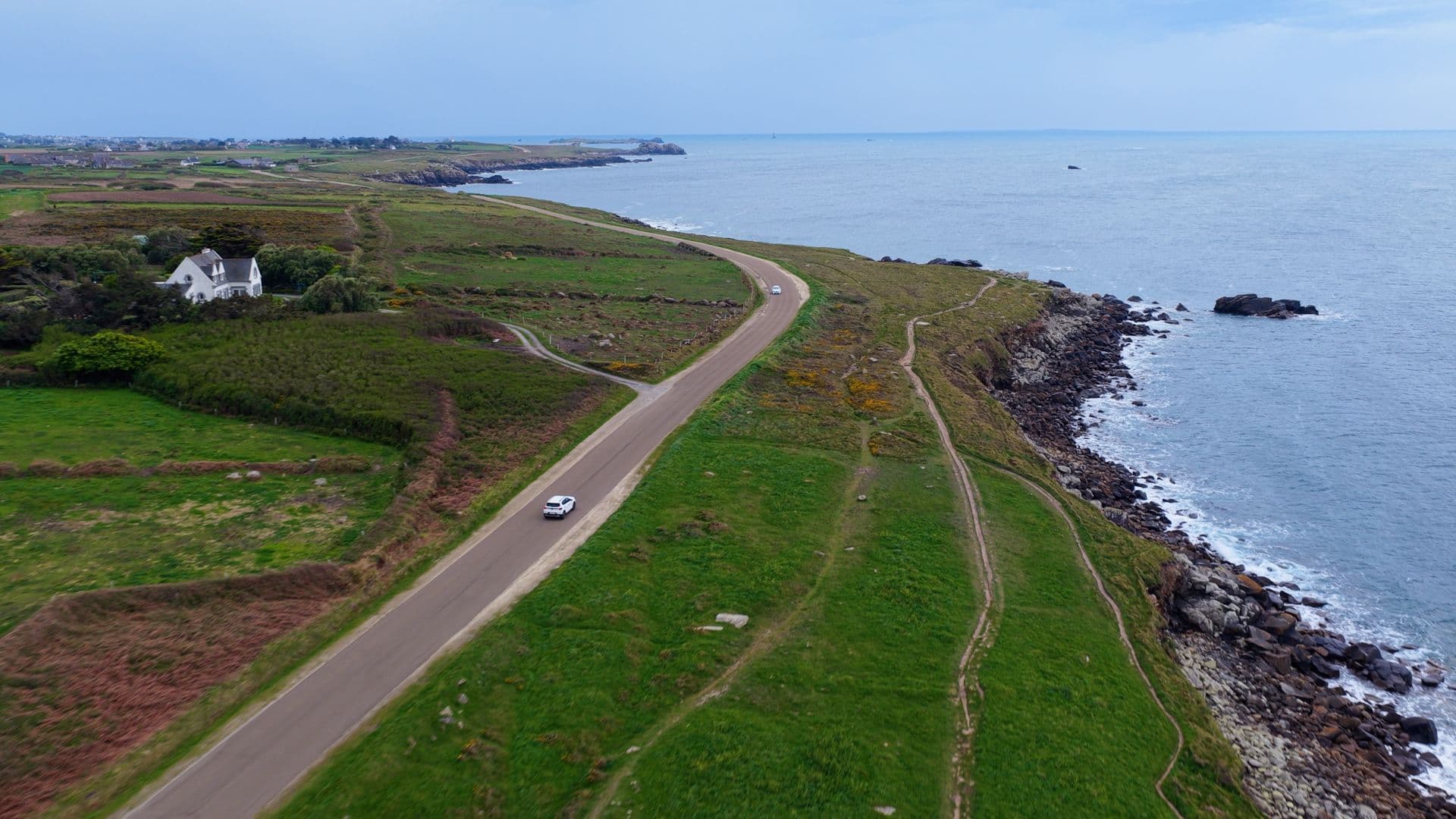 Route côtière sinueuse avec deux voitures près des falaises et de la mer