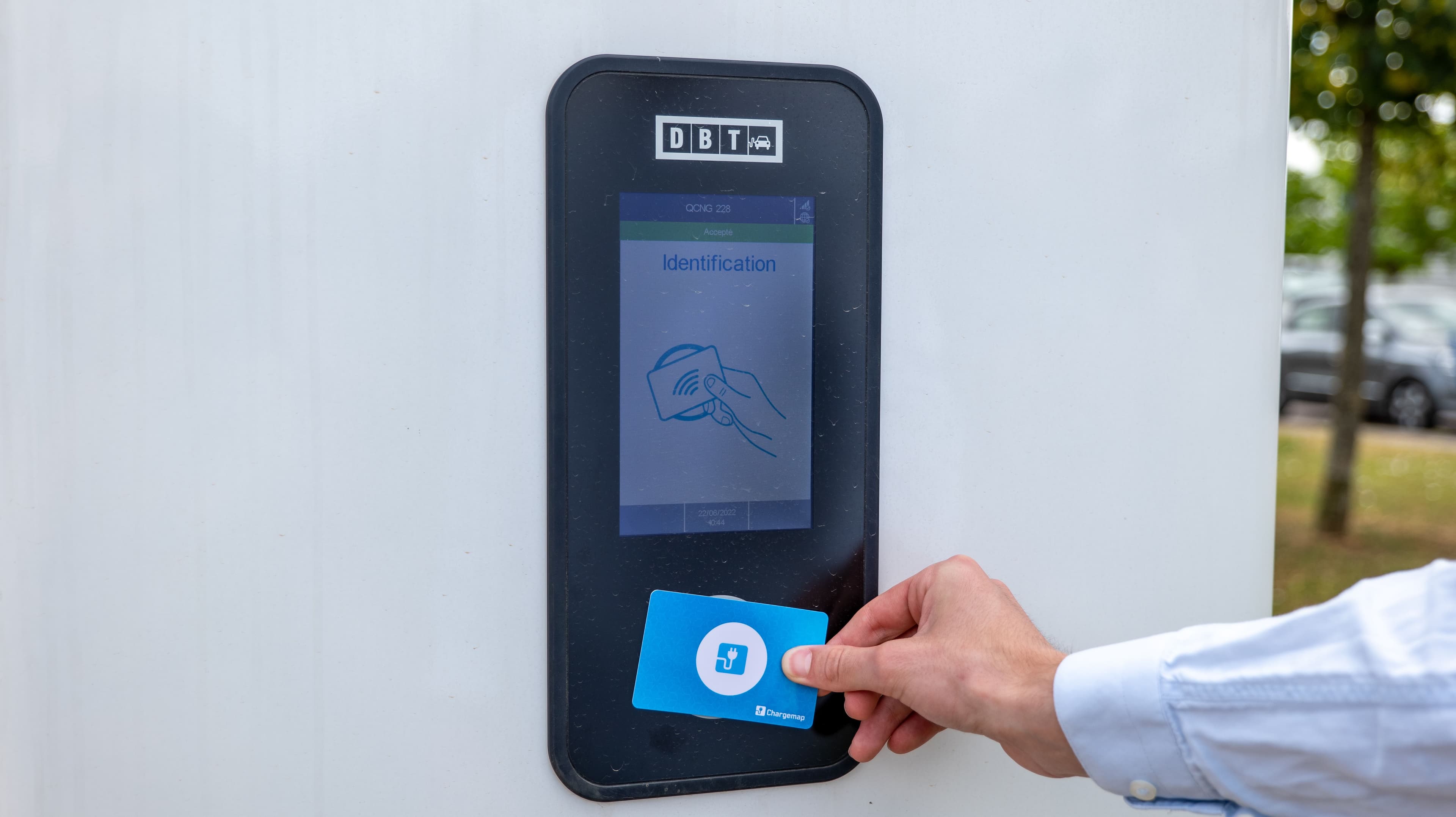Un conducteur de voiture électrique passe son badge de paiement sur une borne de recharge