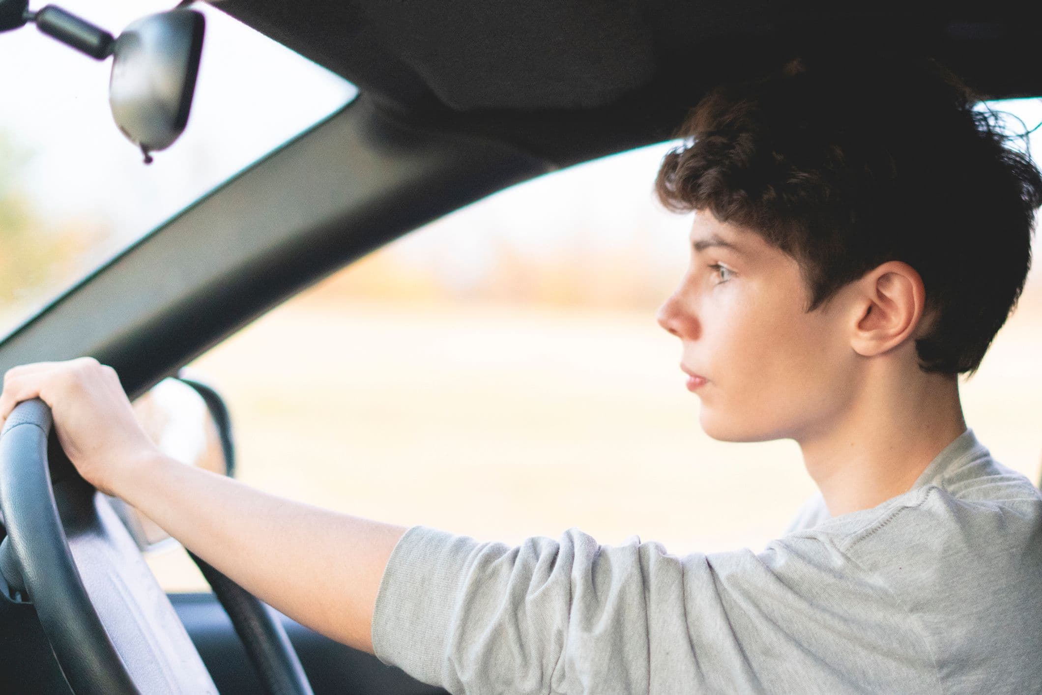 Adolescent conduisant une voiture de profil, mains sur le volant
